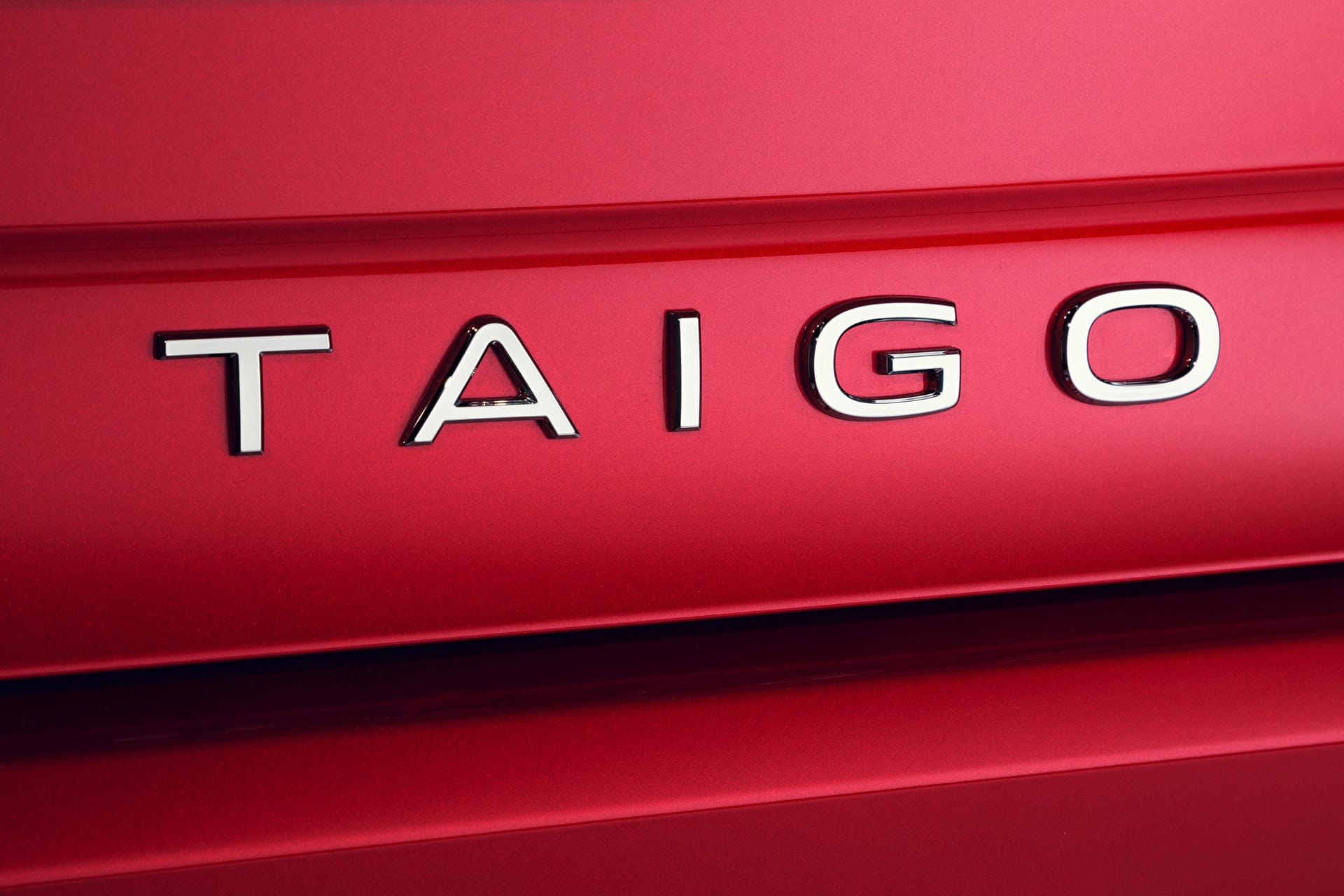 Chromowany napis „TAIGO” na błyszczącym, czerwonym nadwoziu Volkswagena Taigo.
