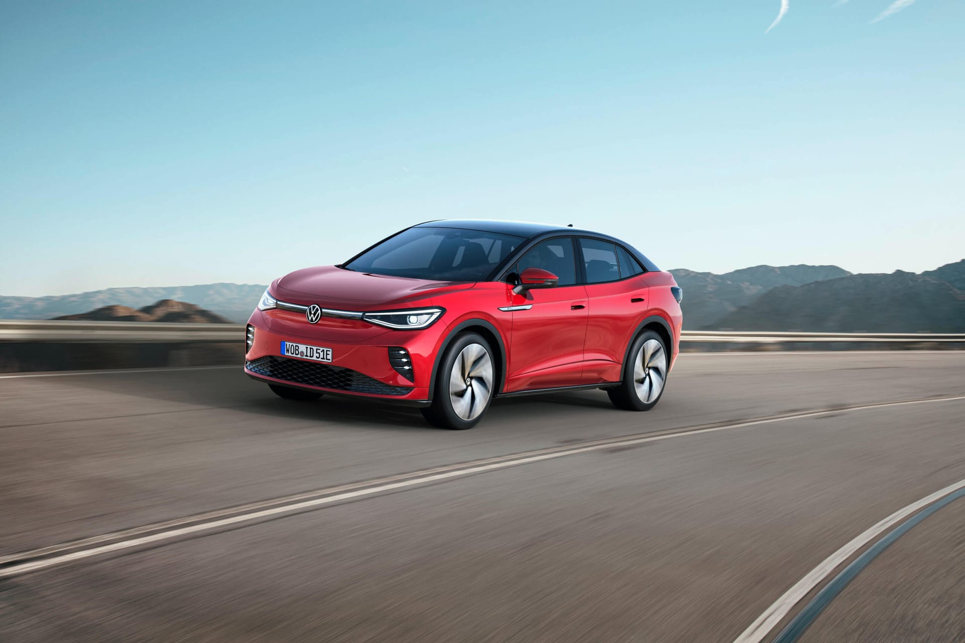 Czerwony Volkswagen ID.5 na zakręcie, w tle góry i błękitne niebo.