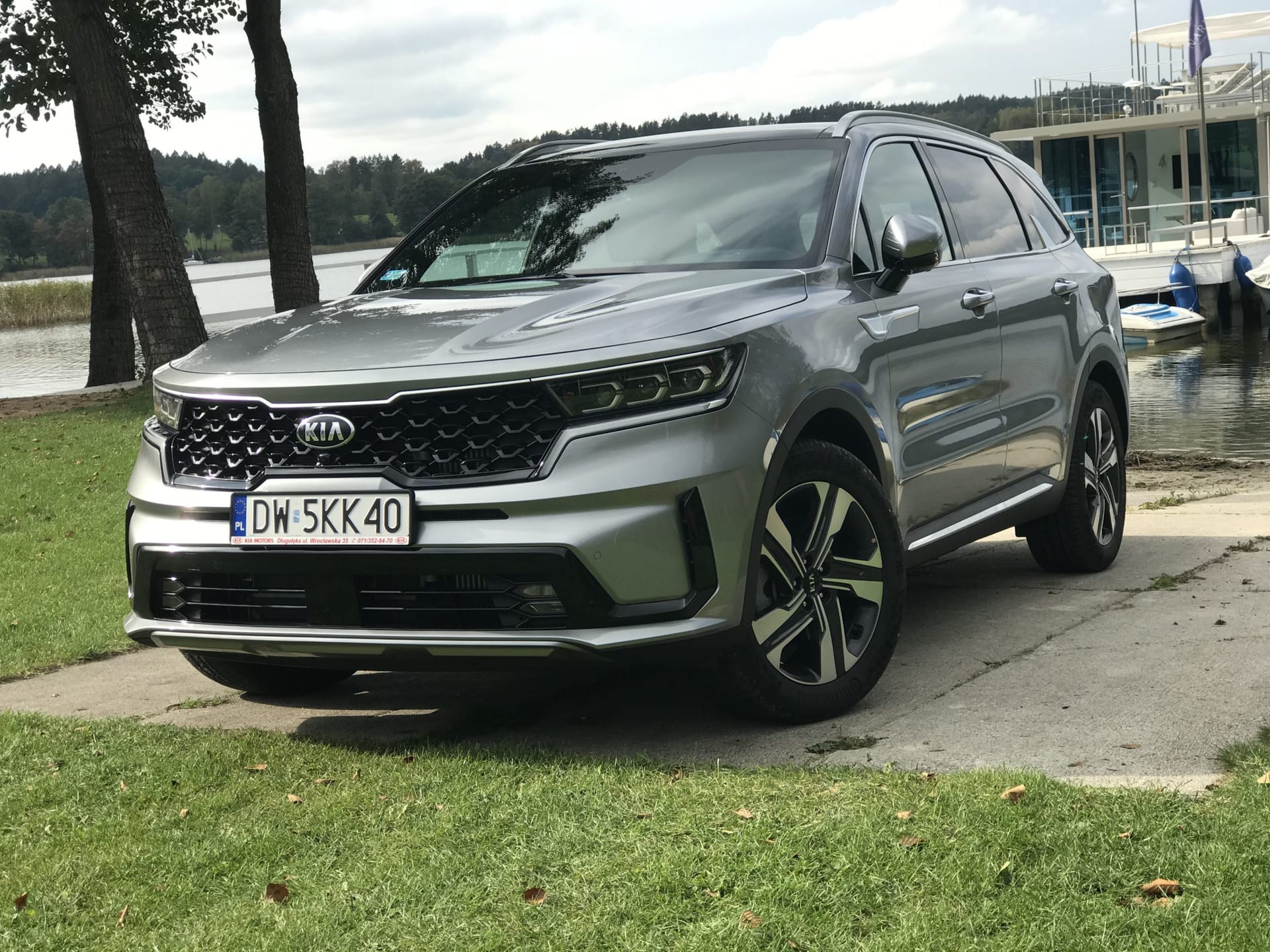 Srebrny Kia Sorento stoi na betonie nad jeziorem, obok trawy, drzew i pomostu.