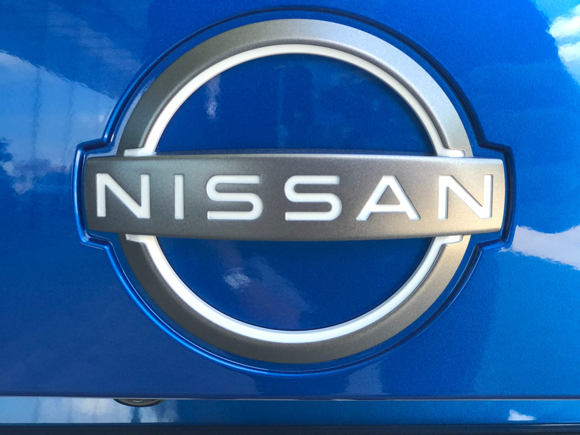 Logo Nissana na metalicznie niebieskim tle, podkreślające styl modelu Juke Hybrid.