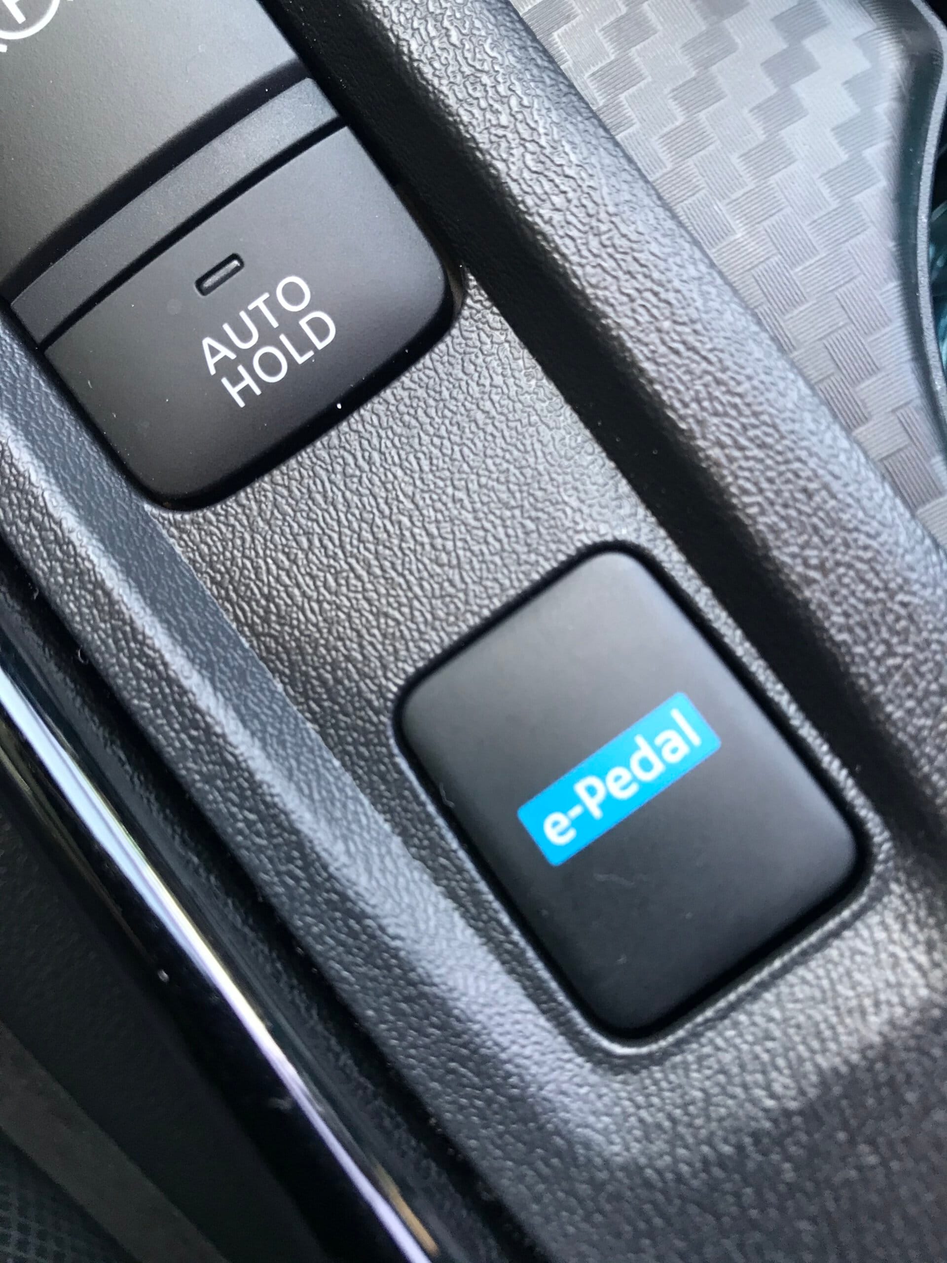 Konsola środkowa w samochodzie Nissan Juke Hybrid z przyciskami AUTO HOLD i e-Pedal na czarnym tle.