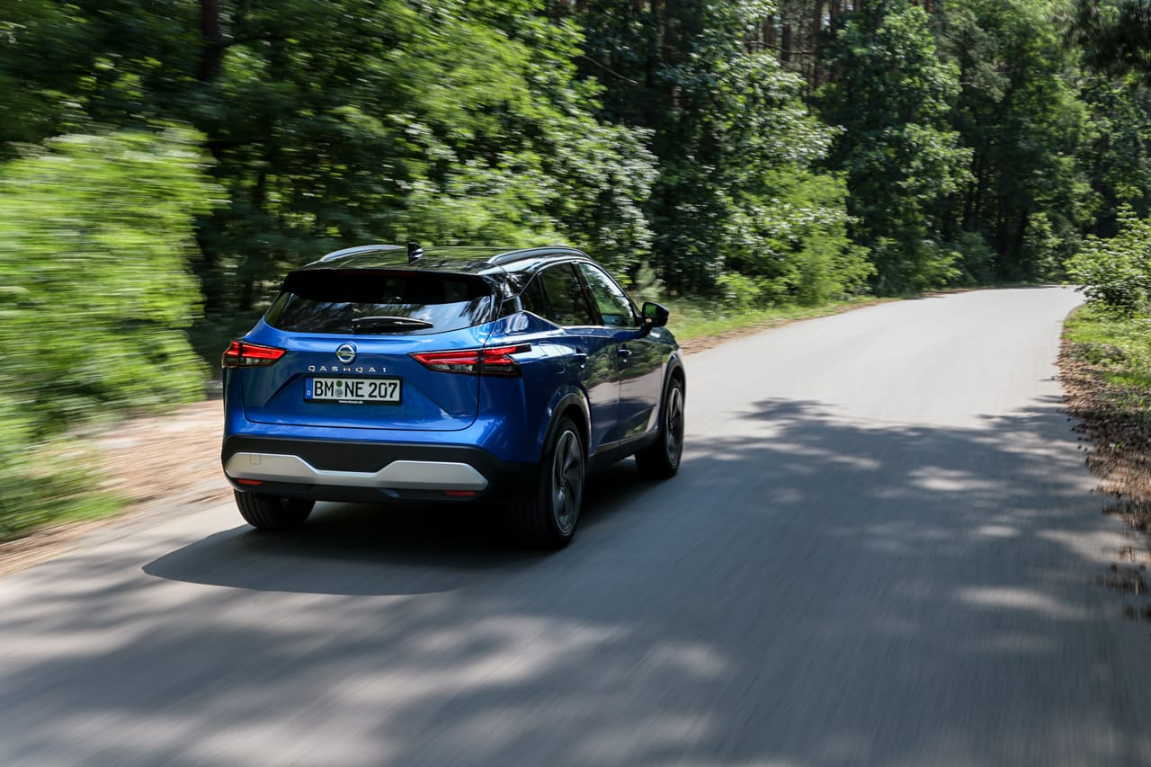 Niebieski Nissan Qashqai jedzie w ciągu dnia po asfaltowej drodze przez zielony las.