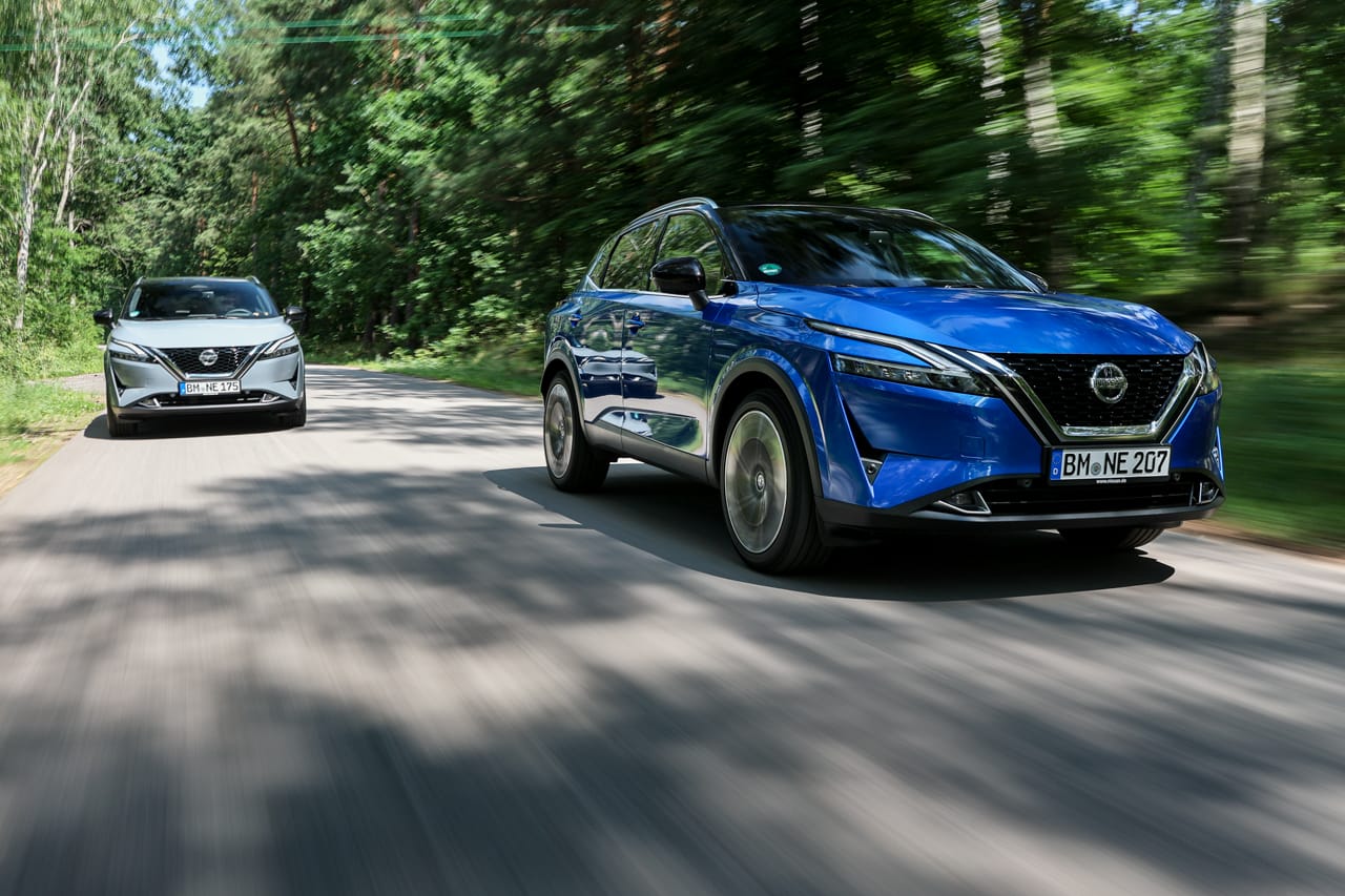 Dwa SUV-y marki Nissan – niebieski i czarny – pędzą alejką wśród drzew.