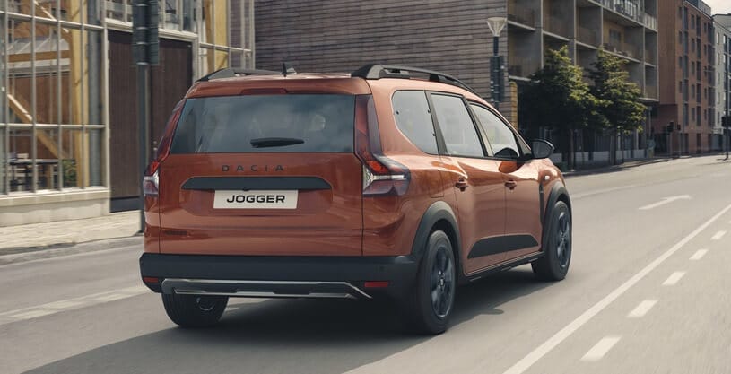 Brązowy Dacia Jogger jedzie ulicą miasta na tle nowoczesnych budynków.