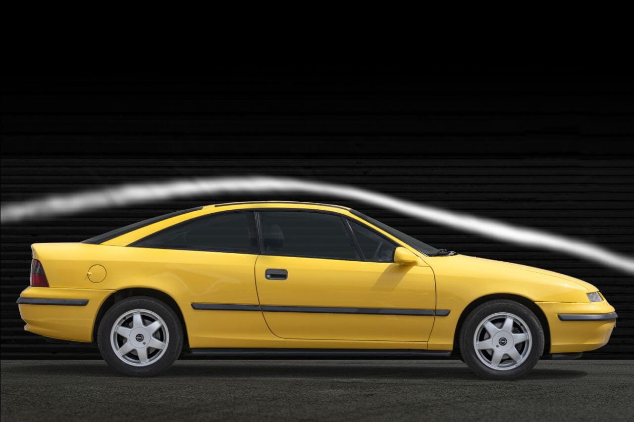 Żółty Opel Calibra na czarnym tle, a nad nim biała linia podkreślająca aerodynamikę.