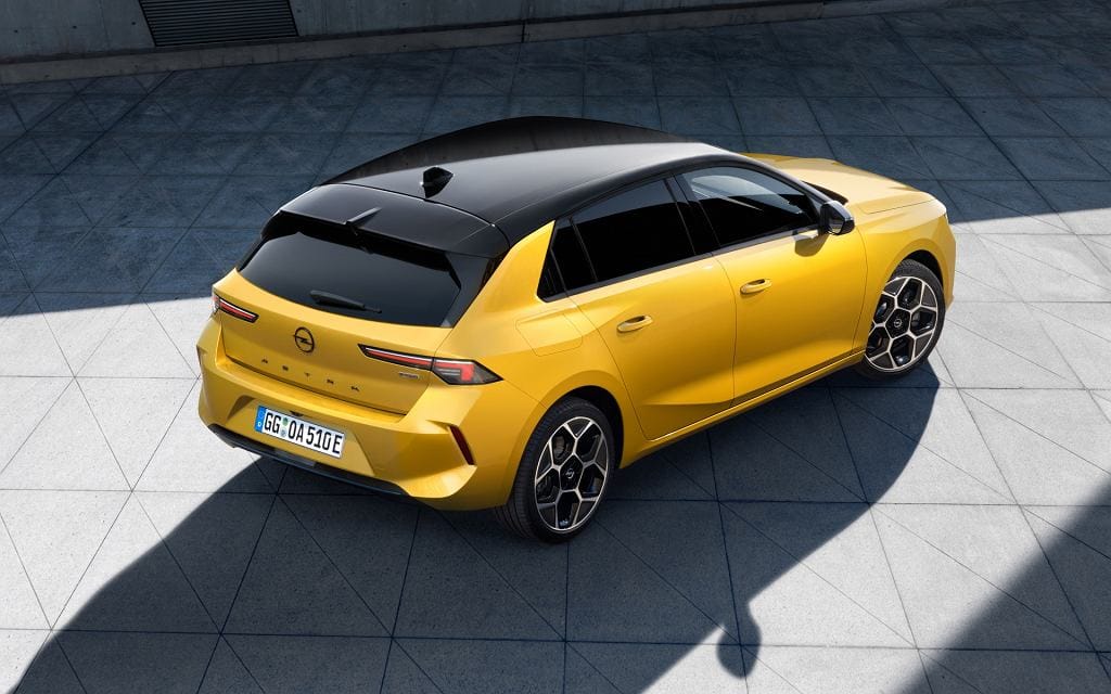 Żółty Opel Astra z czarnym dachem stoi na kafelkach; widok z góry i z tyłu.