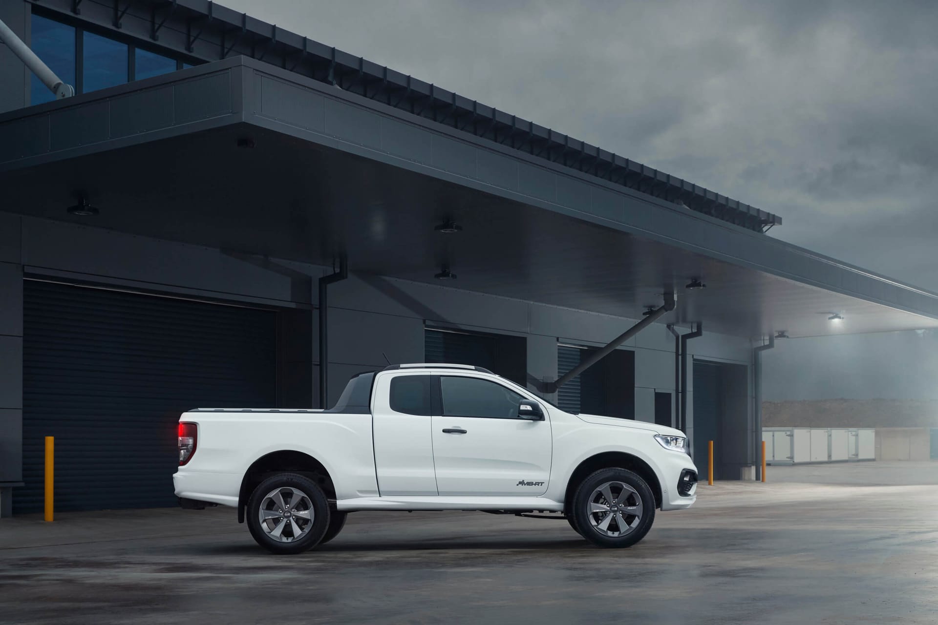 Biały Ford Ranger stoi przed nowoczesnym budynkiem przemysłowym pod zachmurzonym niebem.