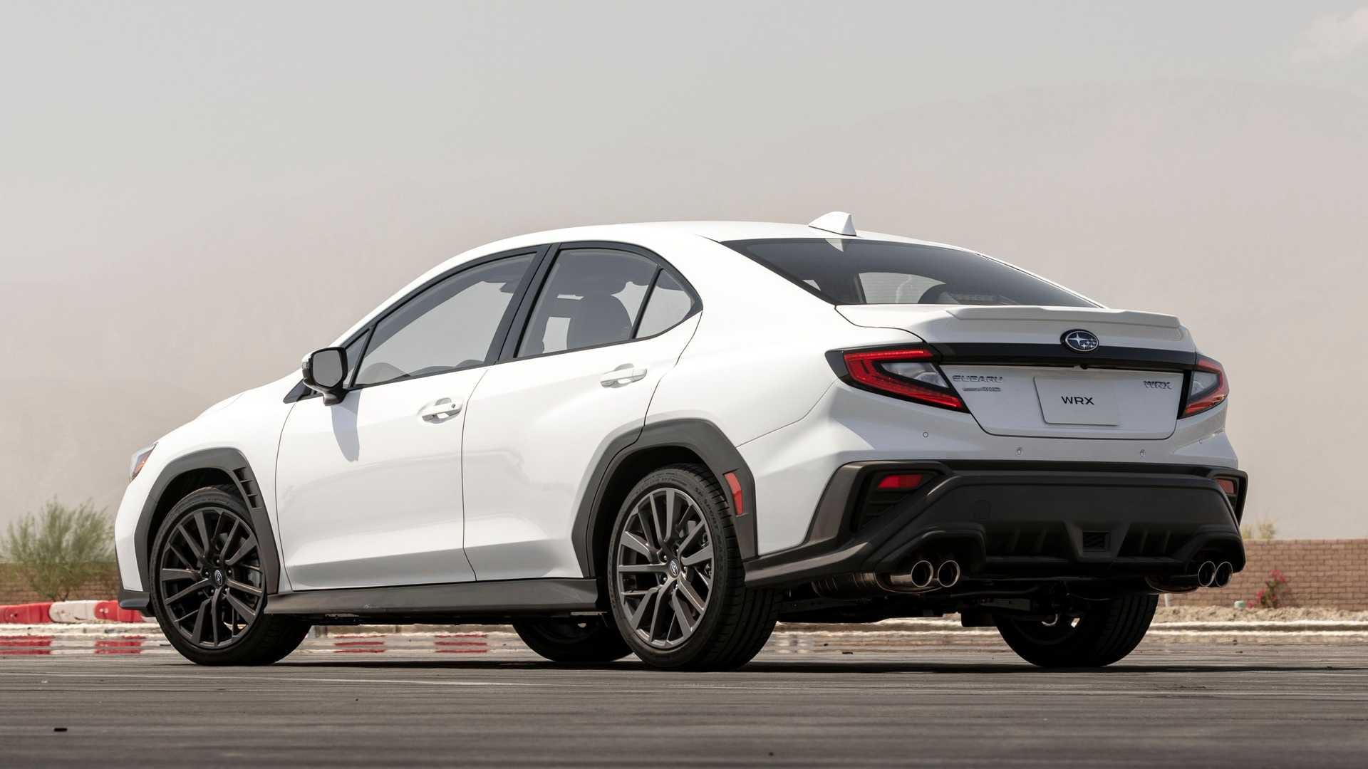 Biały sedan Subaru WRX stoi na utwardzonej nawierzchni; widok z tyłu i z boku.