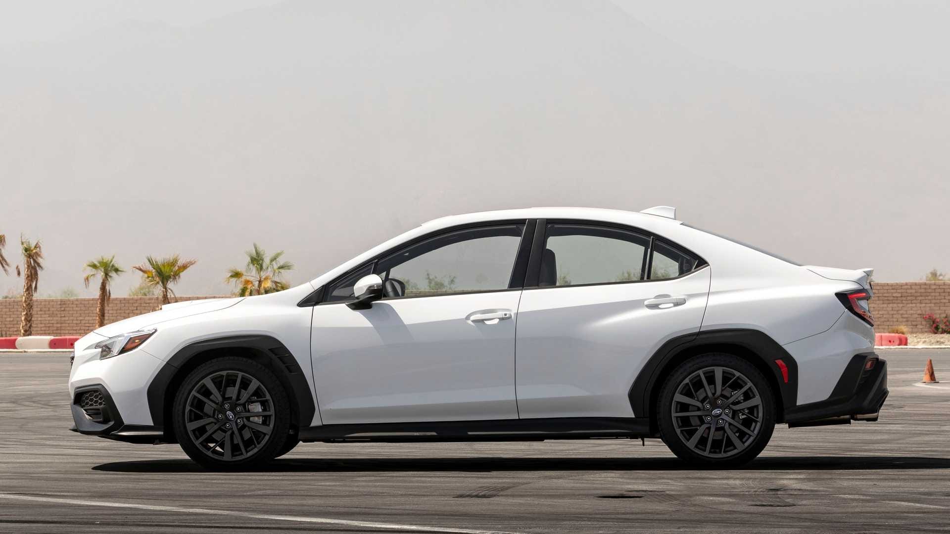 Biały sedan Subaru WRX widziany z profilu na asfalcie, w tle palmy i zamglone niebo.