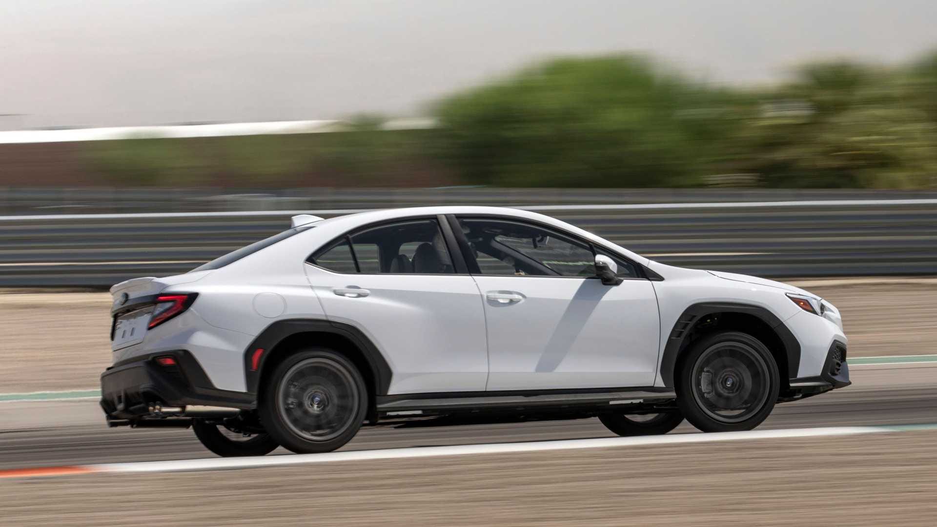 Białe Subaru WRX pędzi po torze wyścigowym, a rozmyte tło podkreśla ruch.