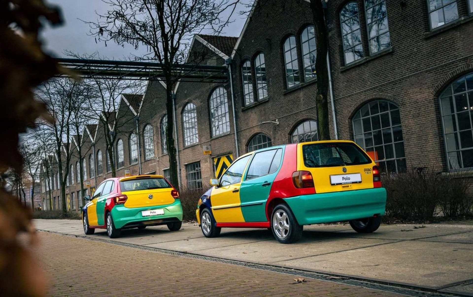 Dwa kolorowe Volkswageny Polo na tle ceglanych budynków przemysłowych.