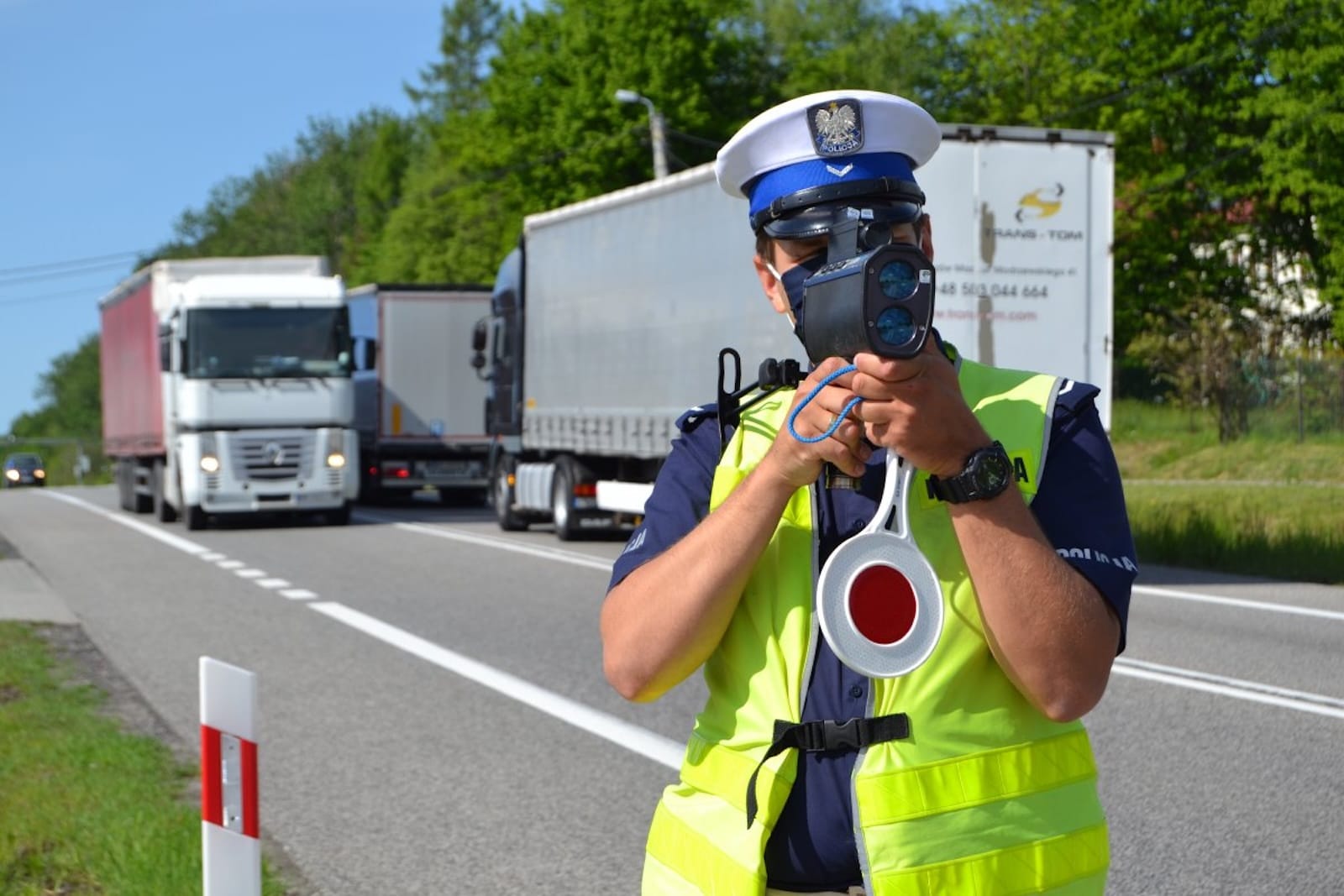 policjant sprawdza prędkość miernikiem laserowym na drodze poza obszarem zabudowanym