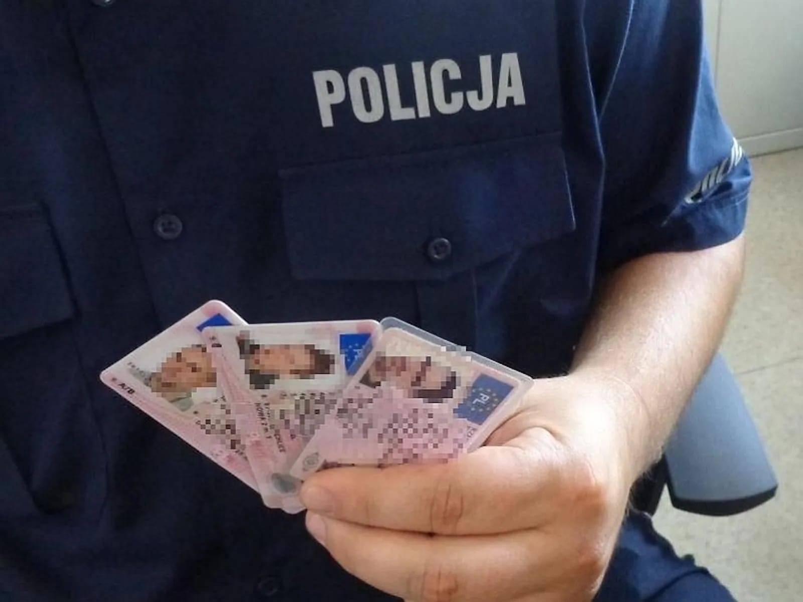 policjant trzyma w ręku 3 dokumenty prawa jazdy