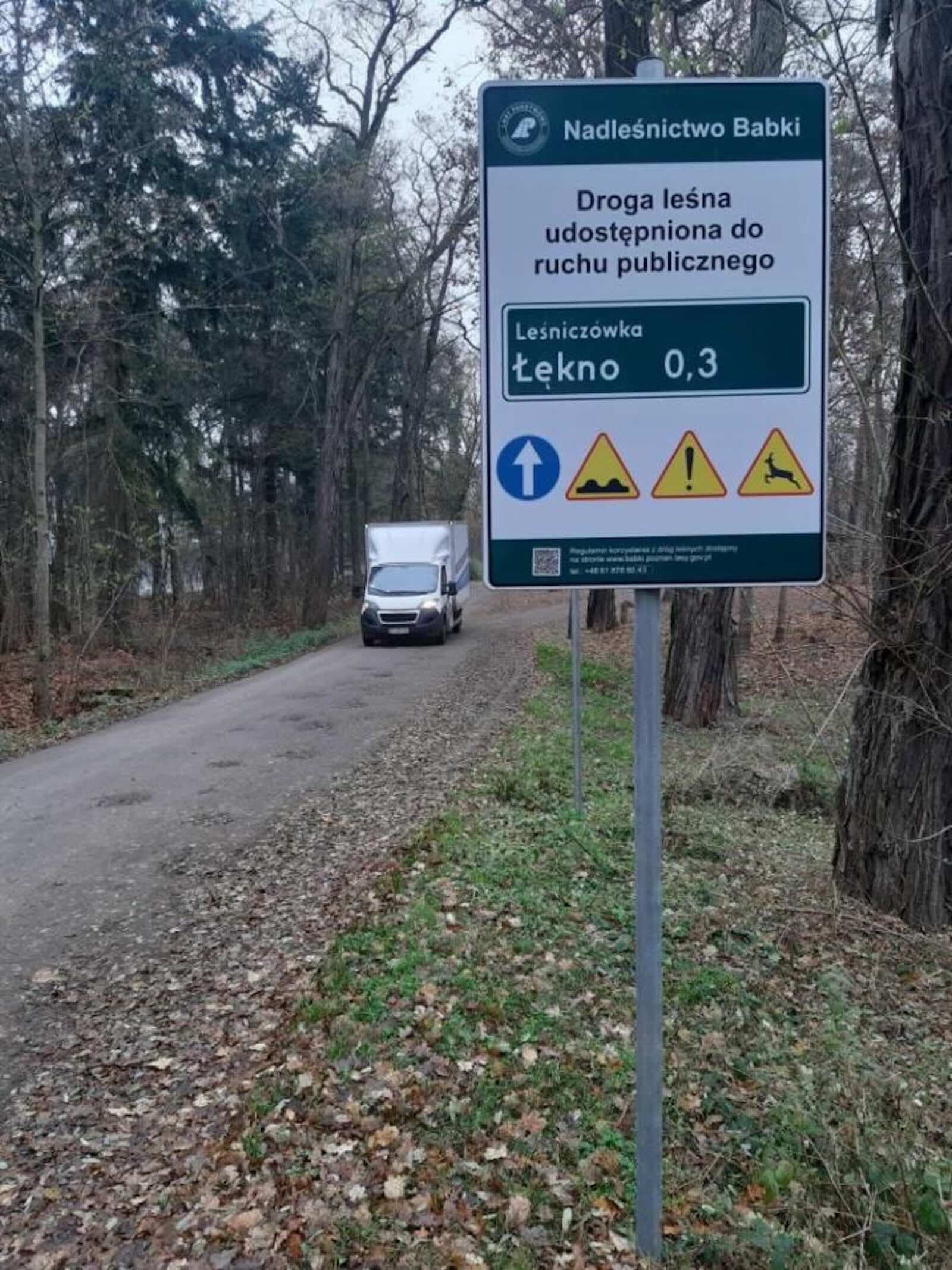 tablica droga leśna udostępniona dla ruchu w tle samochód jadący przez las