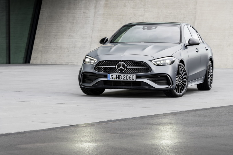 Srebrny Mercedes klasy C stoi na płytach przed nowoczesnym betonowym budynkiem.