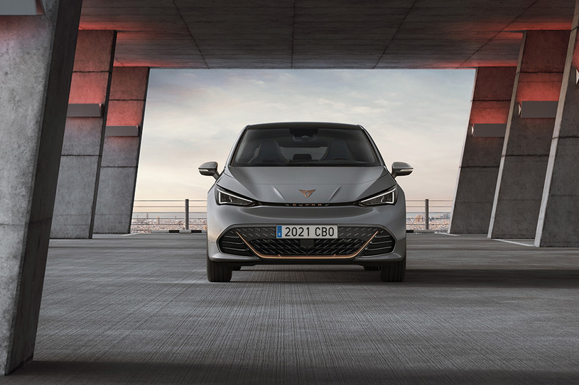 Srebrny Cupra Born z tablicą rejestracyjną 2021 CBO pod nowoczesną betonową konstrukcją, widok z przodu.