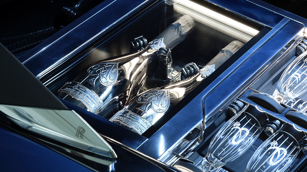 Dwie butelki szampana i cztery grawerowane kieliszki w luksusowym wnętrzu Rolls-Royce’a.