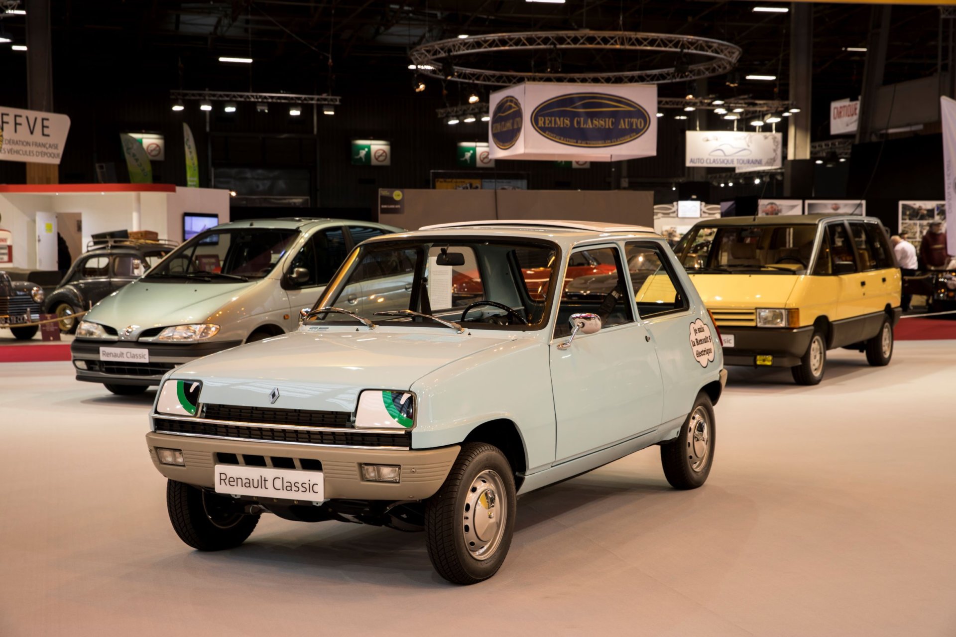 Jasnoniebieski, klasyczny Renault 5 na wystawie samochodów, a w tle inne zabytkowe modele Renault.