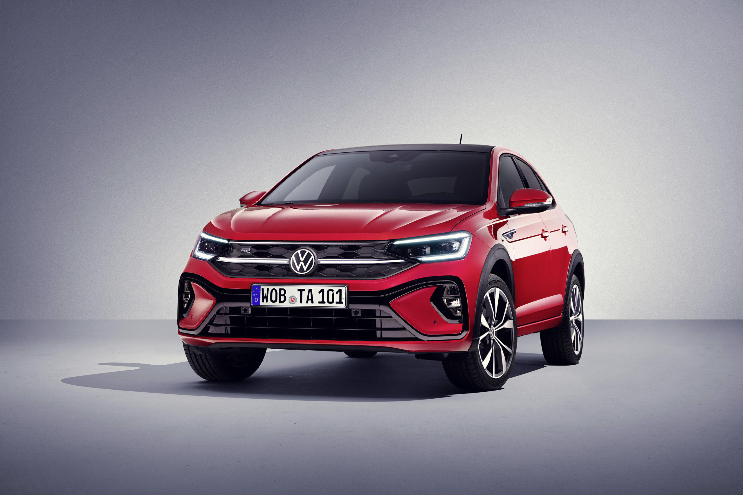 Czerwony SUV Volkswagen Taigo stoi w studiu na szarym tle, przodem skierowanym w prawo.