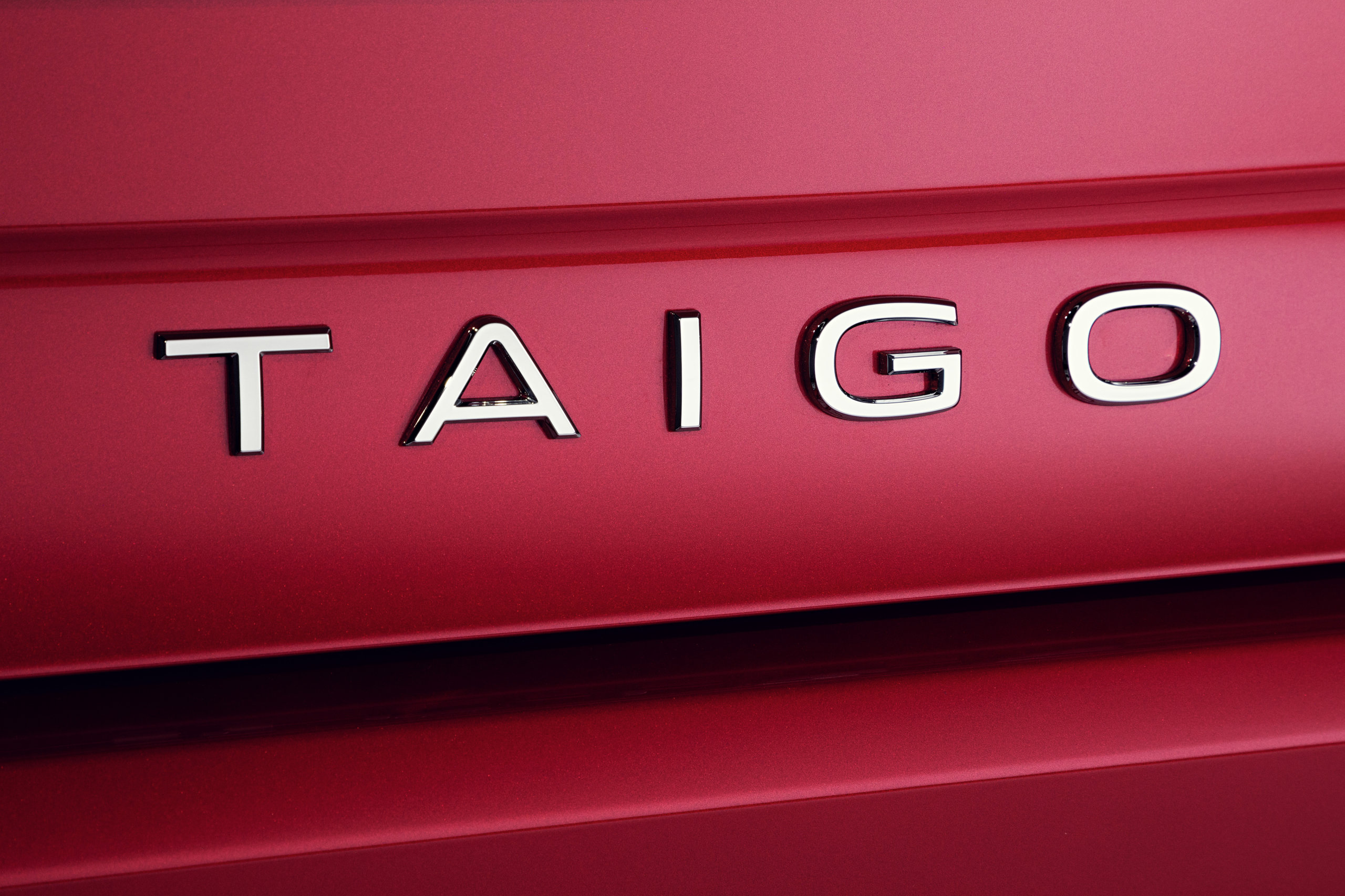 Chromowany napis „TAIGO” na błyszczącym, czerwonym nadwoziu Volkswagena Taigo.