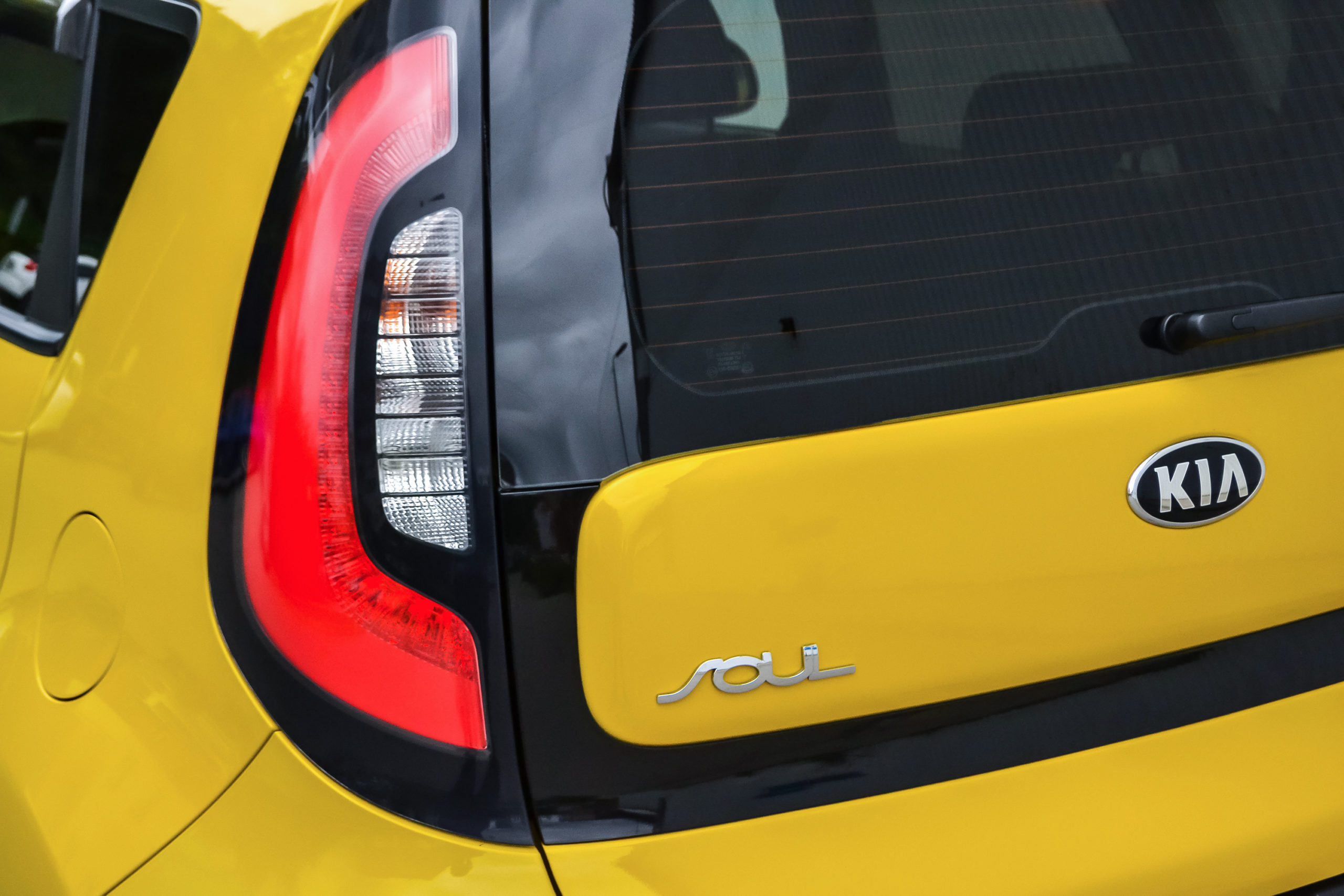 Tył żółtego Kia Soul z lewym światłem, tylną szybą, logo Kia i emblematem Soul.