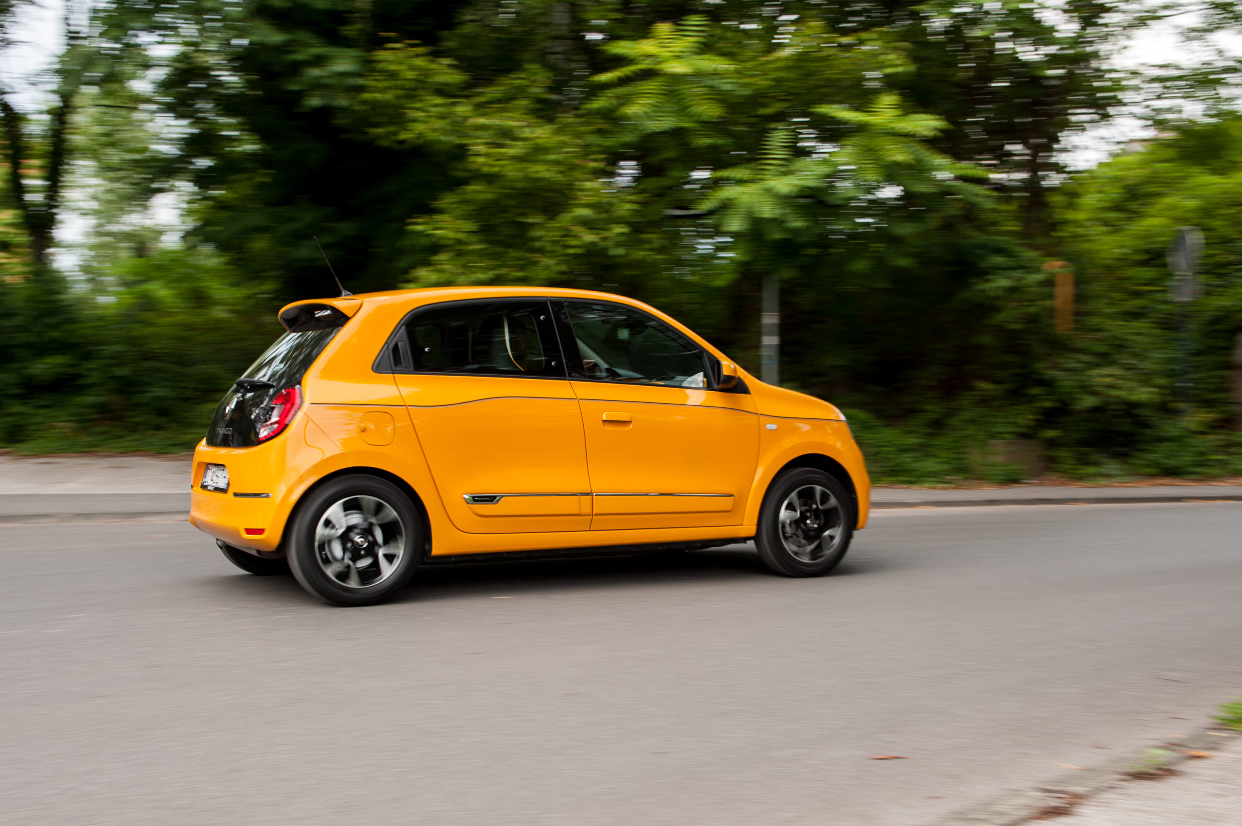 Żółte Renault Twingo jedzie po gładkiej drodze, a w tle widać drzewa i zieleń.