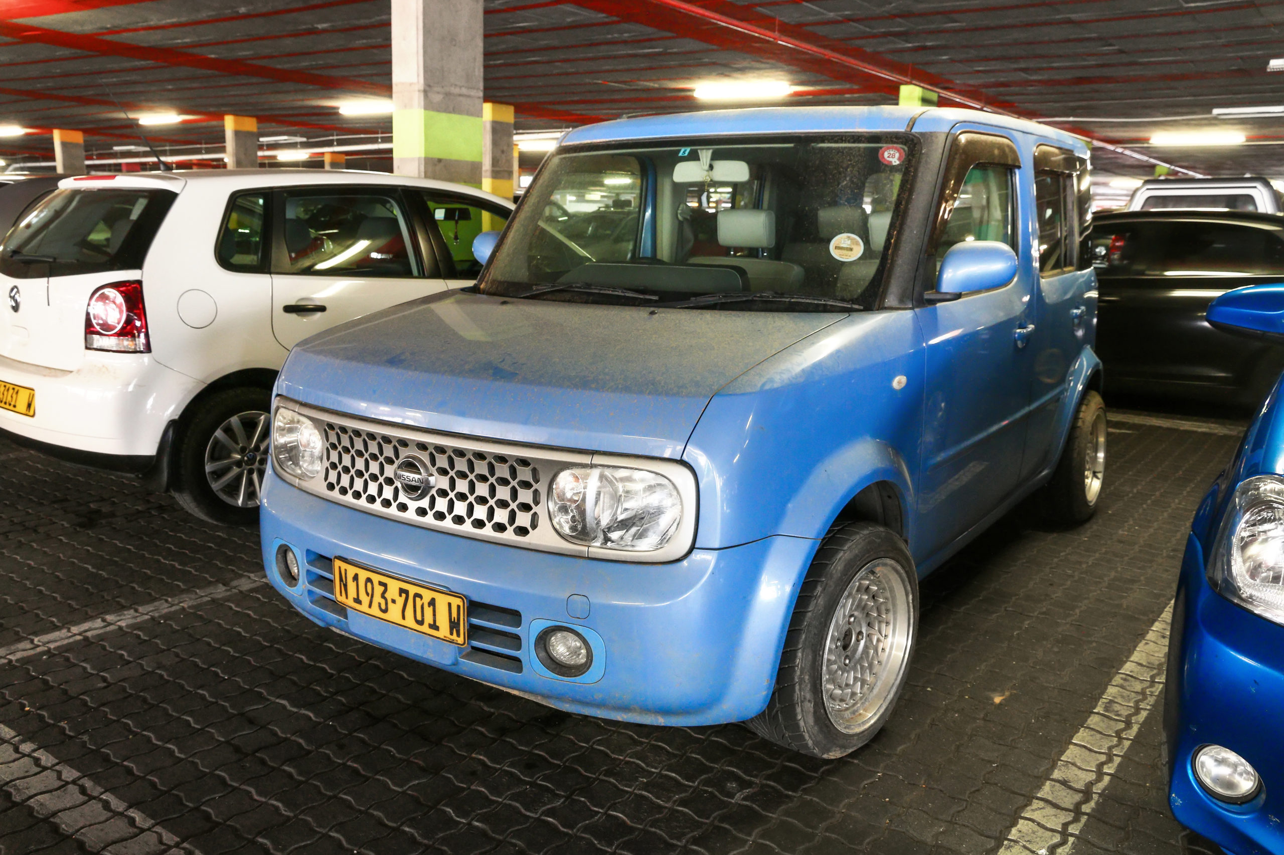 Niebieski Nissan Cube z namibijską tablicą rejestracyjną stoi w garażu obok innych samochodów.