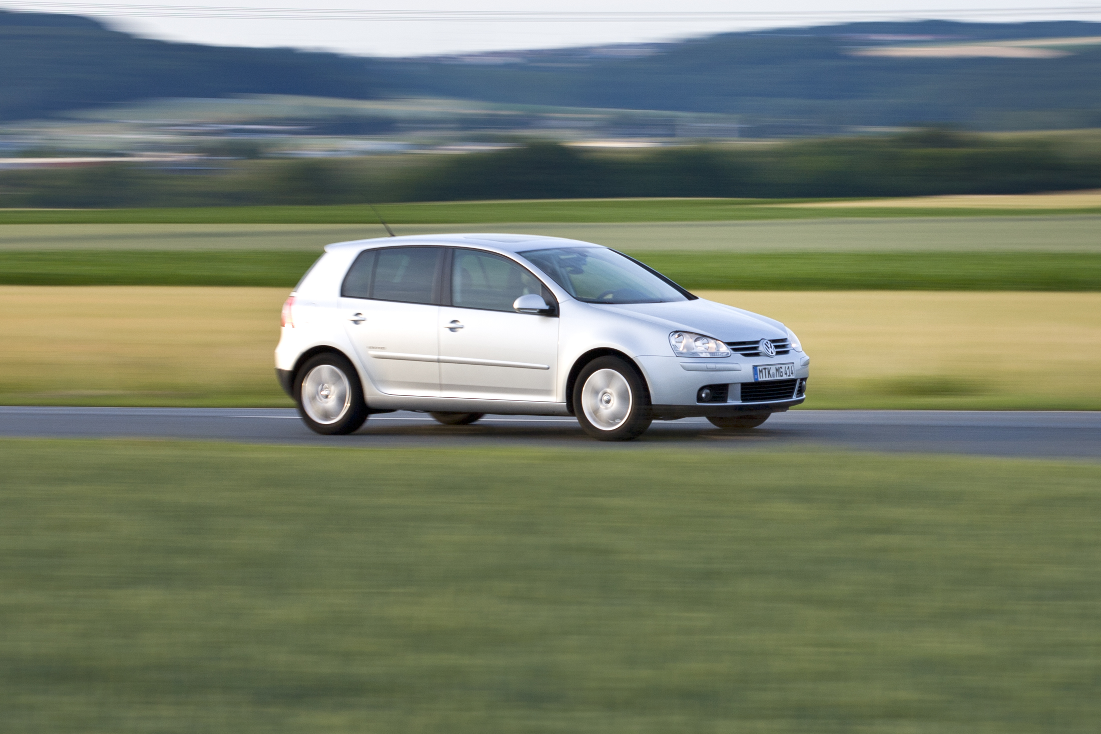 Srebrny Volkswagen Golf V pędzi przez zielone pola, a w tle widać rozmyty ruch.