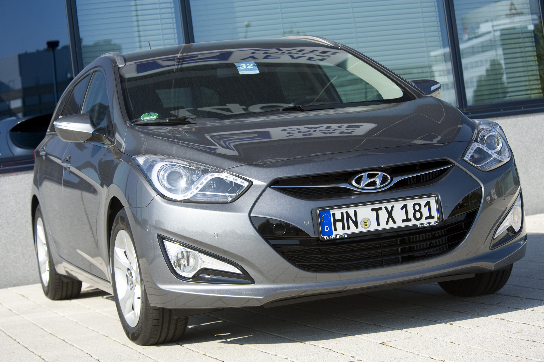 Szary Hyundai i40 z nadwoziem typu hatchback stoi na kostce brukowej przed budynkiem ze szklanymi oknami.