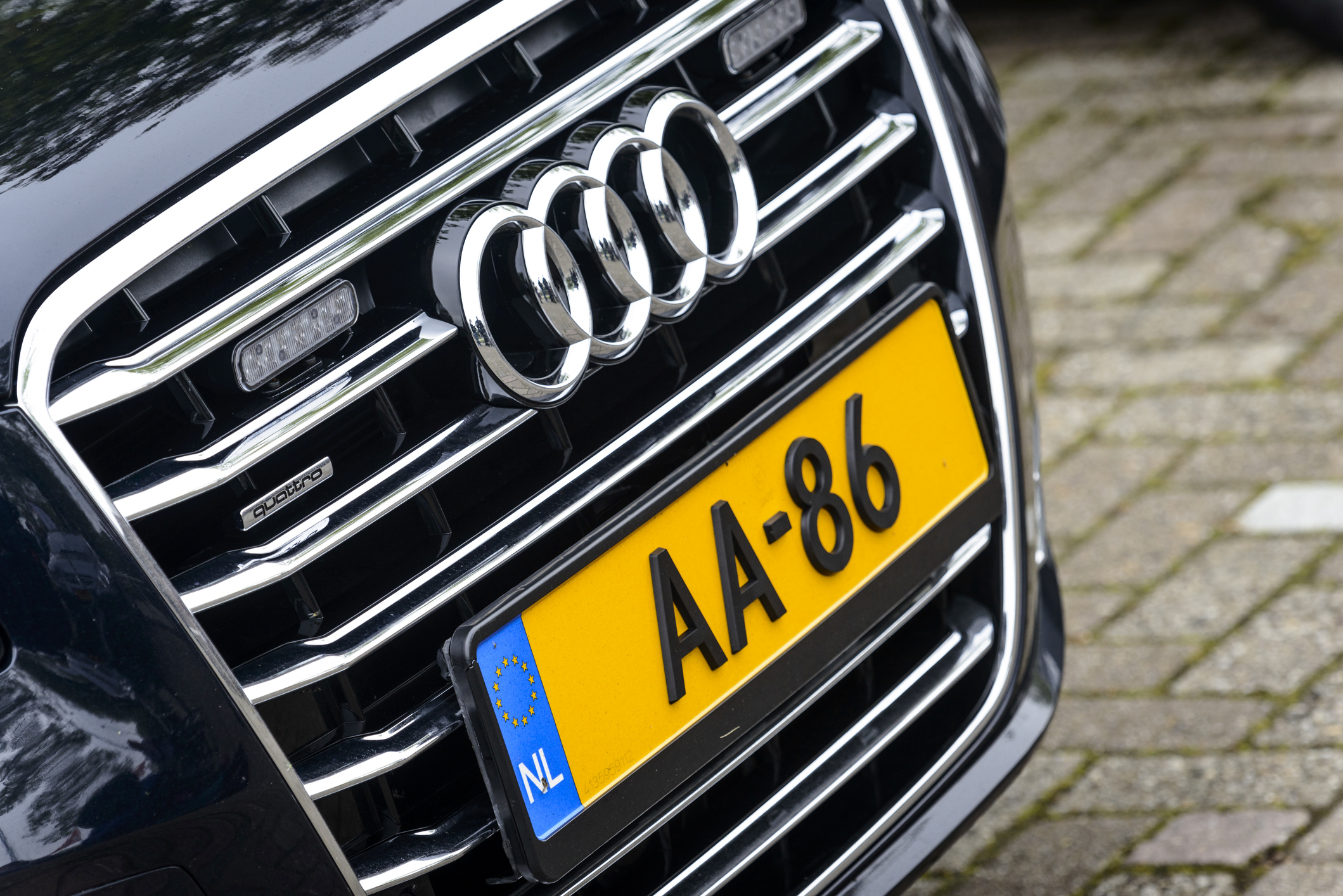 Czarny Audi A8 z żółtą tablicą rejestracyjną AA-86 na ceglanej nawierzchni.