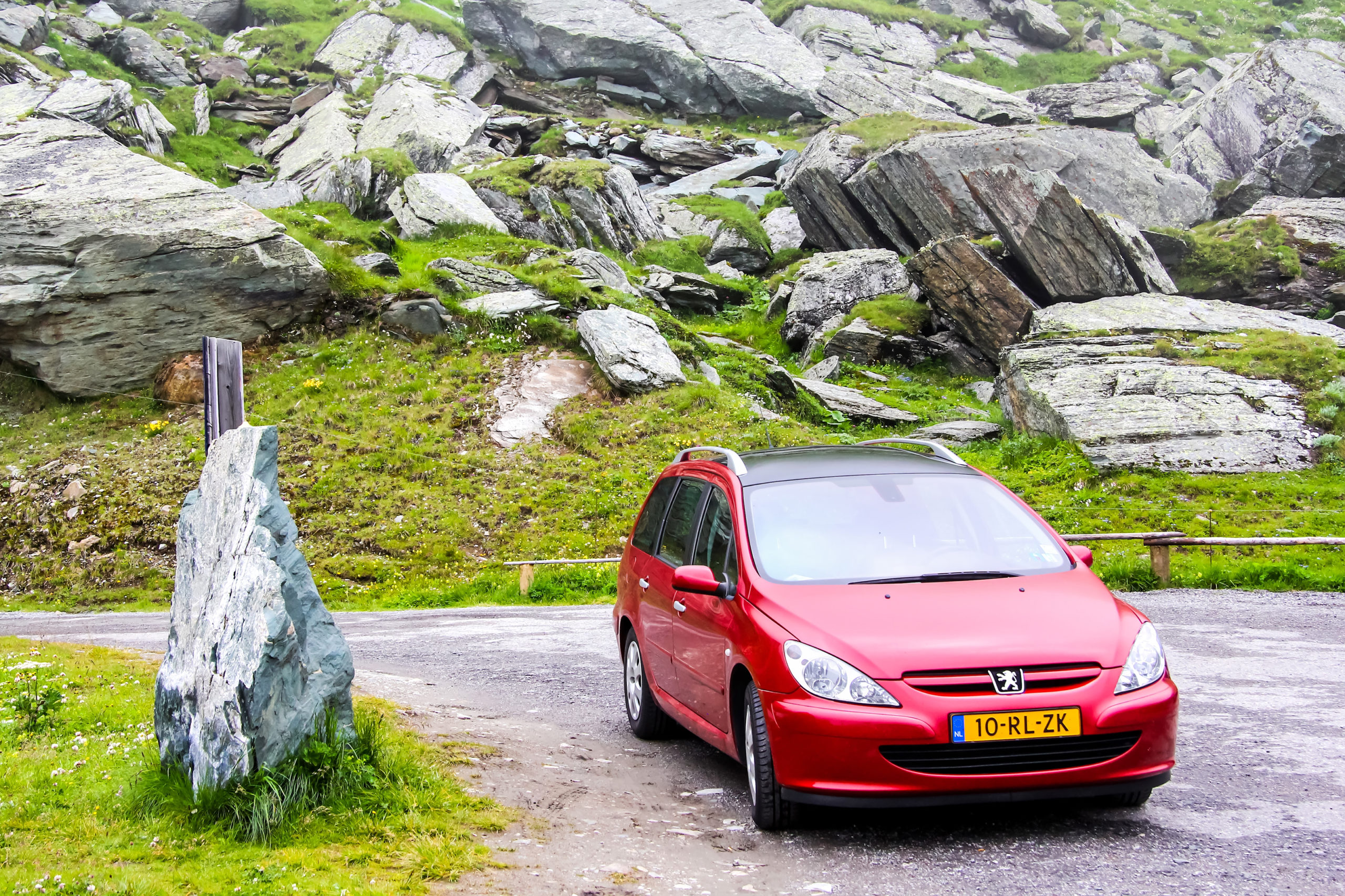 Czerwony Peugeot 307 kombi na poboczu drogi, w otoczeniu skalistych wzgórz i zielonej trawy.