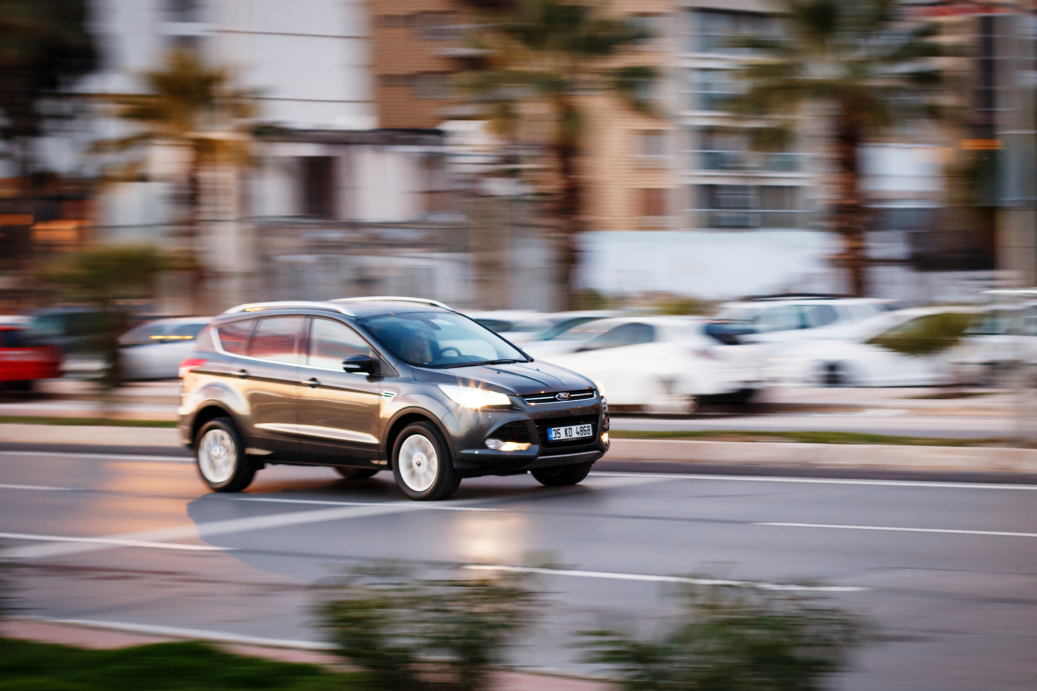 Czarny Ford Kuga MK1 jedzie ulicą miasta, a w tle widać palmy i budynki.