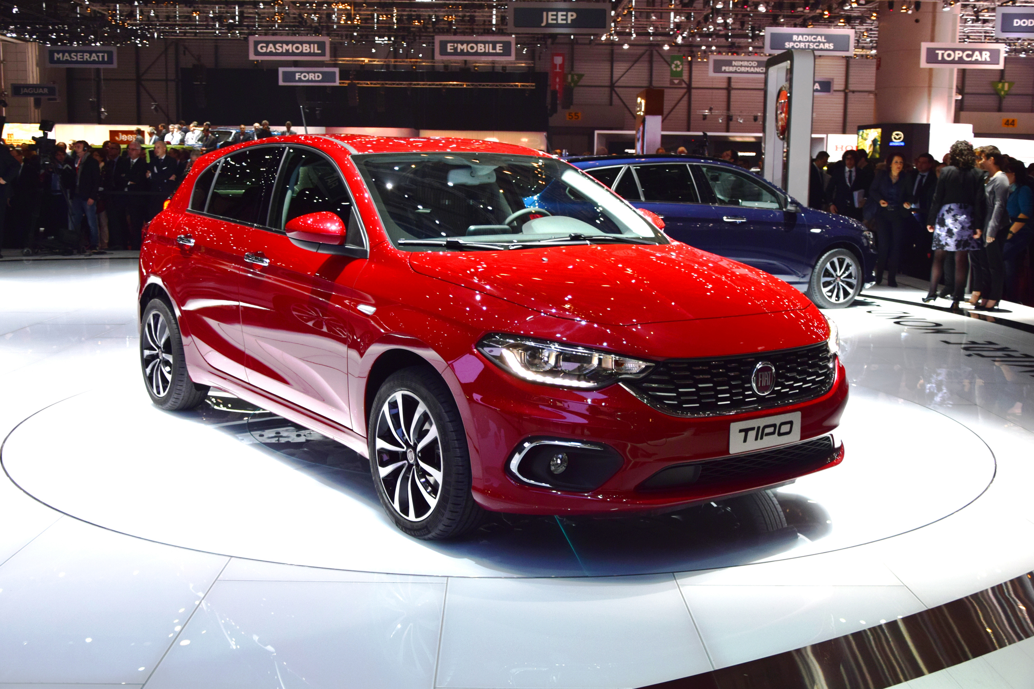 Czerwony Fiat Tipo na białym okrągłym podwyższeniu, w tle ludzie i logo marki.