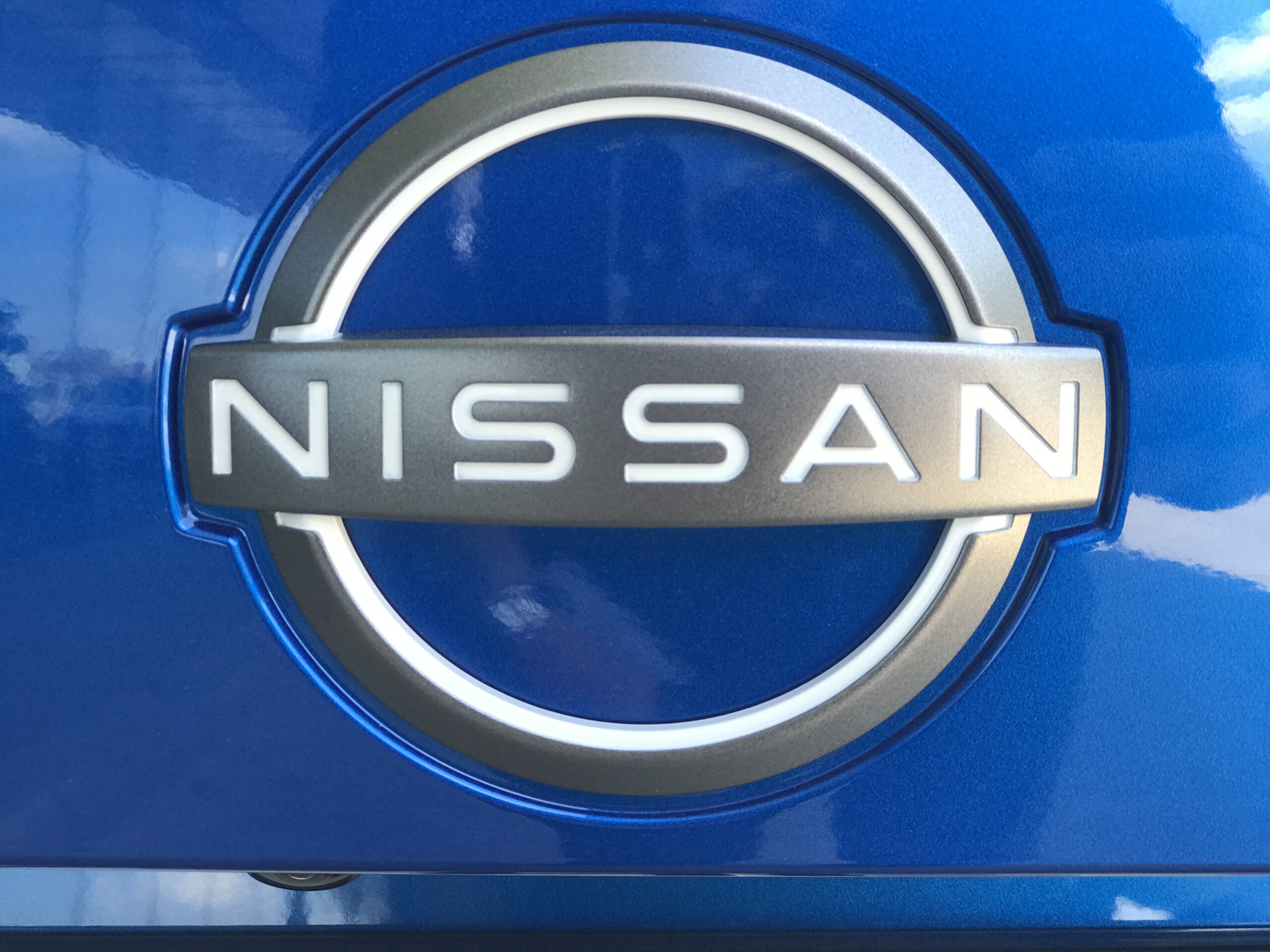 Logo Nissana na metalicznie niebieskim tle, podkreślające styl modelu Juke Hybrid.