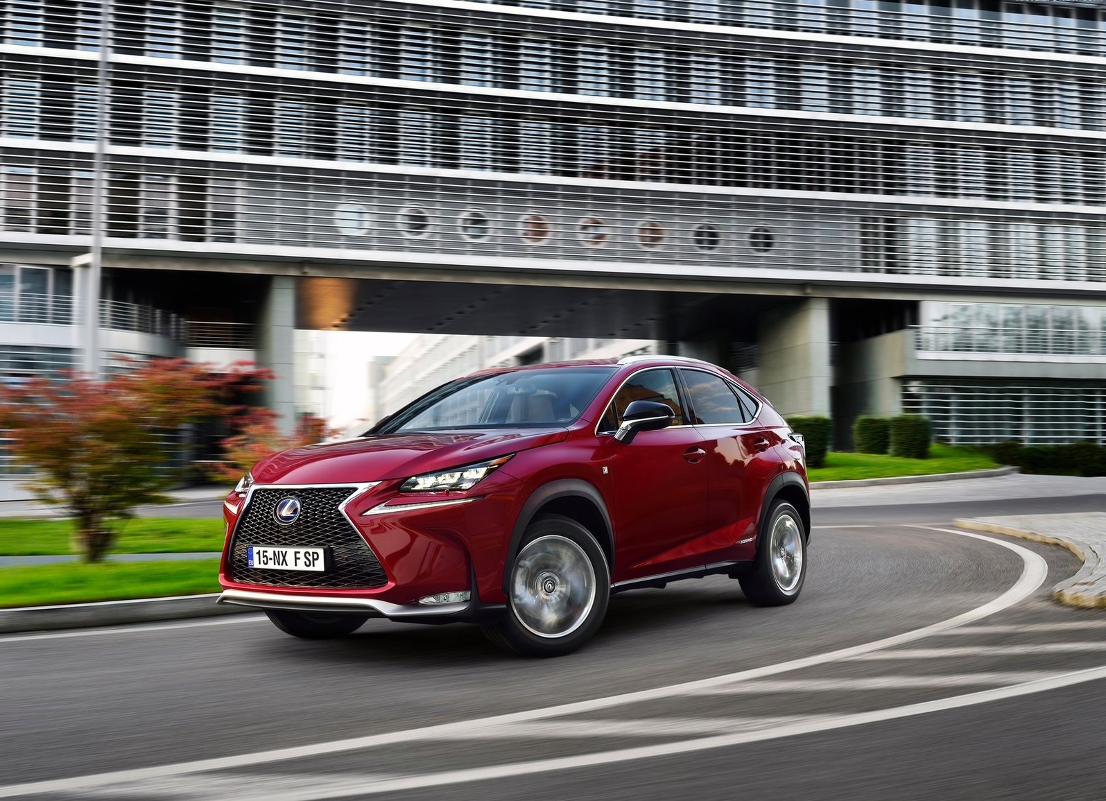 Czerwony Lexus NX pokonuje zakręt w mieście, a w tle widać nowoczesny, przeszklony budynek.