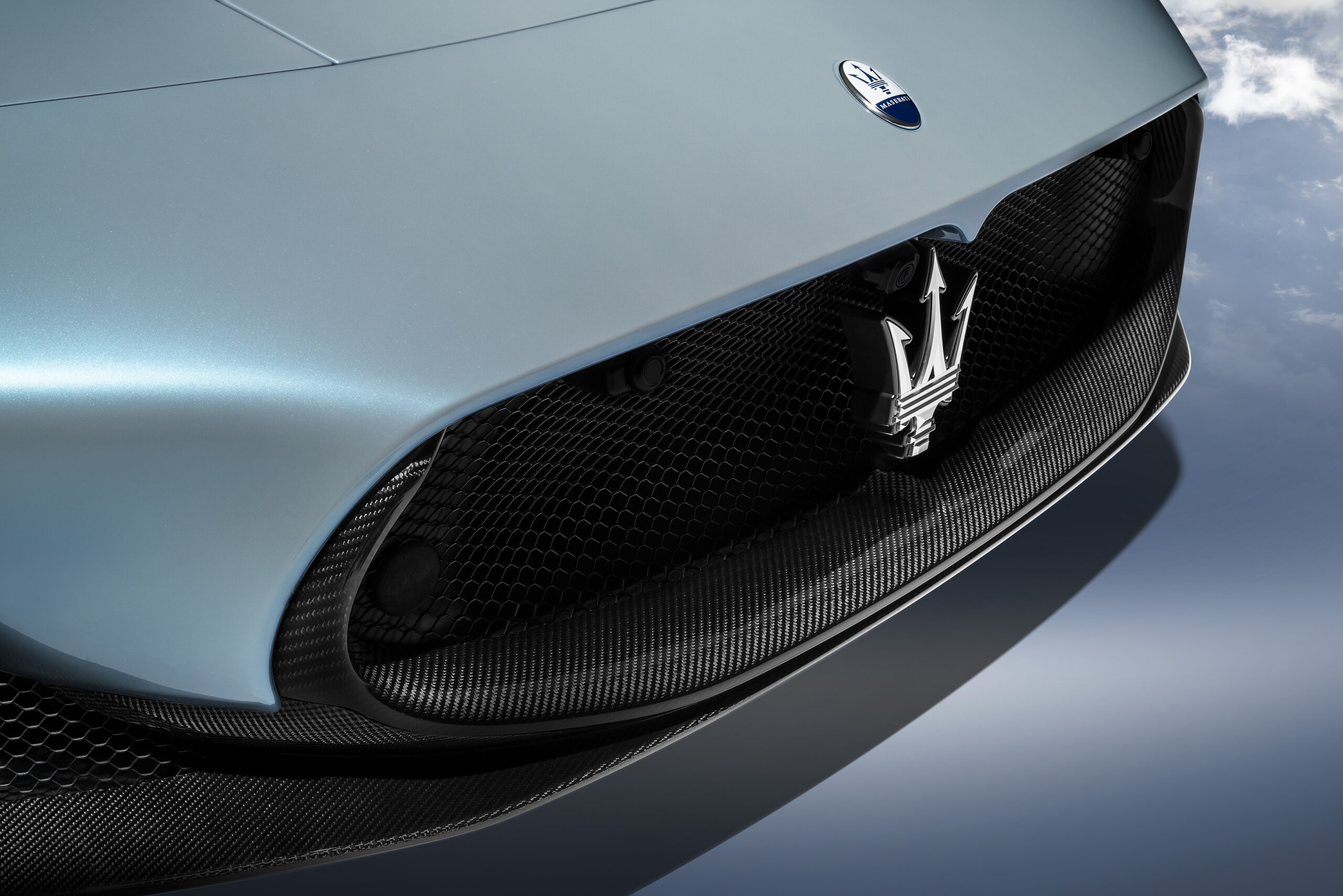 Zbliżenie na grill Maserati MC20 ze srebrnym trójzębem i niebieskim lakierem.