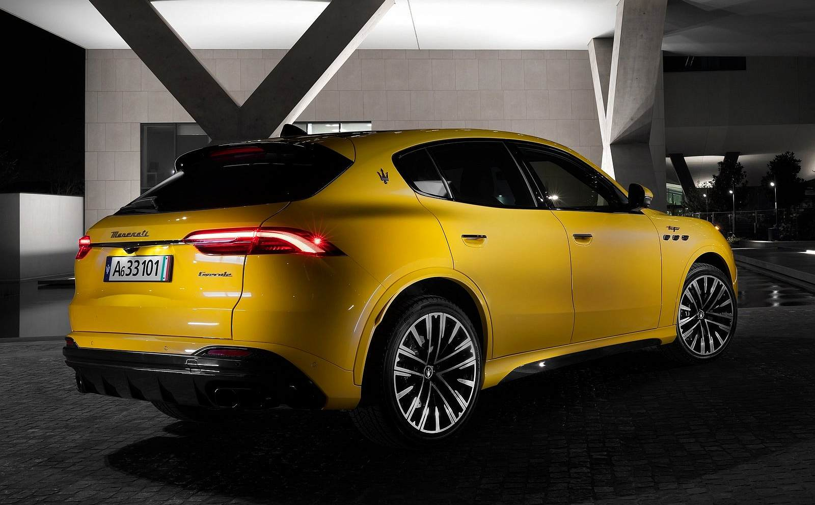 Żółty SUV Maserati Grecale stoi nocą przed nowoczesnym budynkiem w świetle latarni.