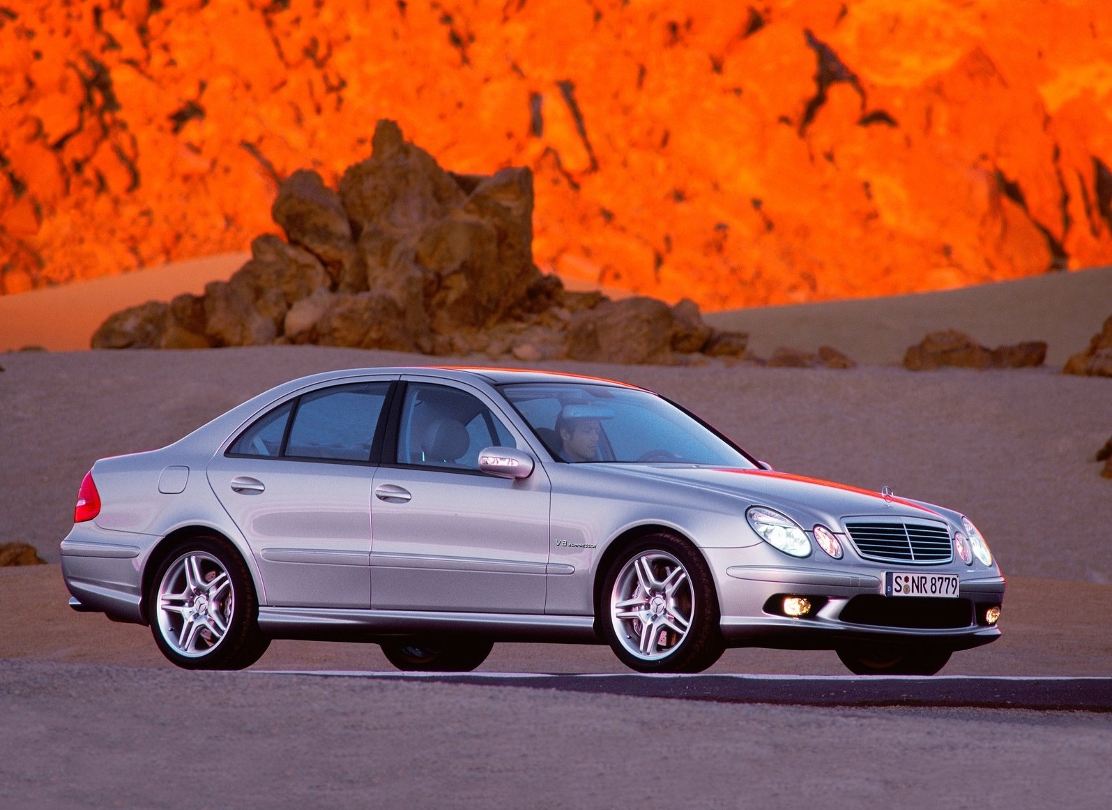Srebrny Mercedes klasy E (W211) na drodze, w tle skały i pomarańczowy klif.
