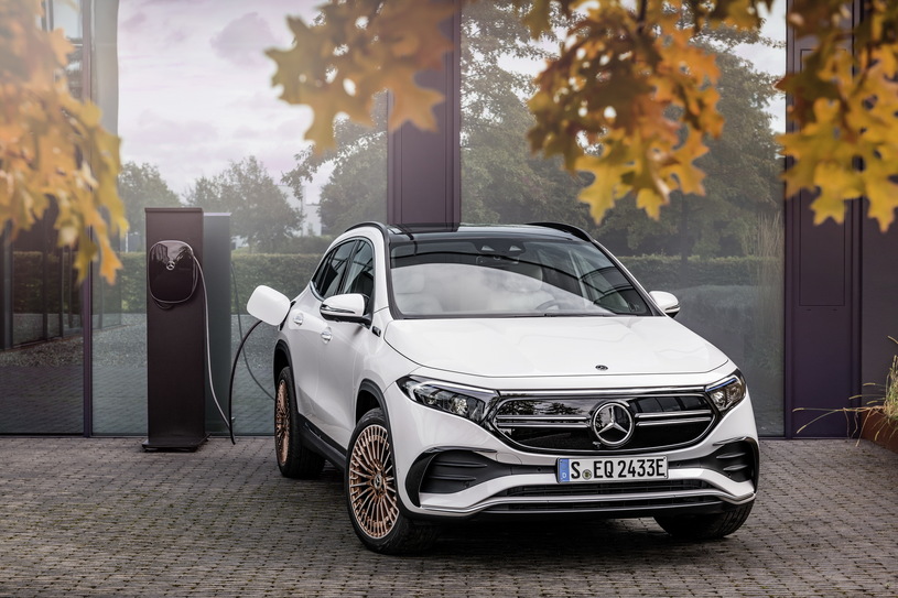 Biały Mercedes EQA ładuje się na zewnątrz, a w tle widać drzewa i szklany budynek.