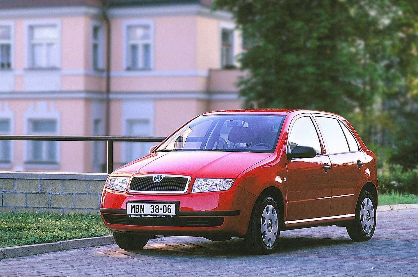 Czerwony hatchback Skoda Fabia stoi na kostce brukowej przy budynku mieszkalnym i zieleni.