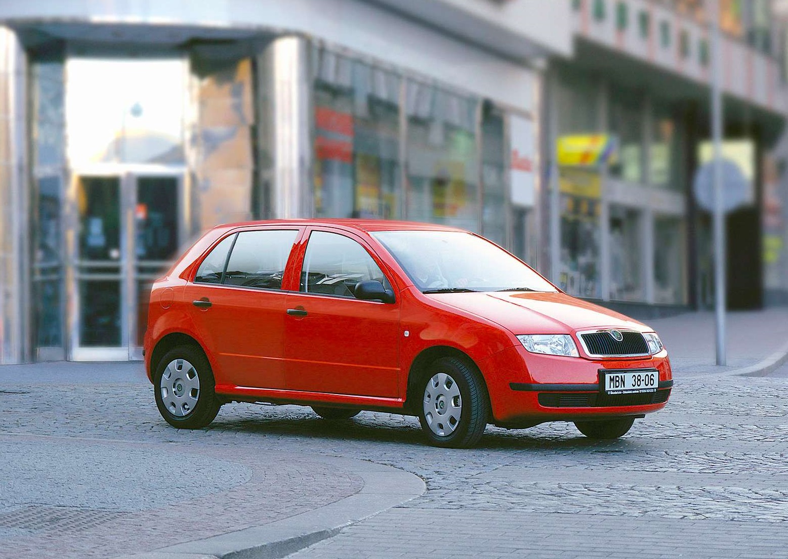 Czerwony hatchback marki Škoda Fabia zaparkowany na ulicy przed przeszklonym budynkiem.