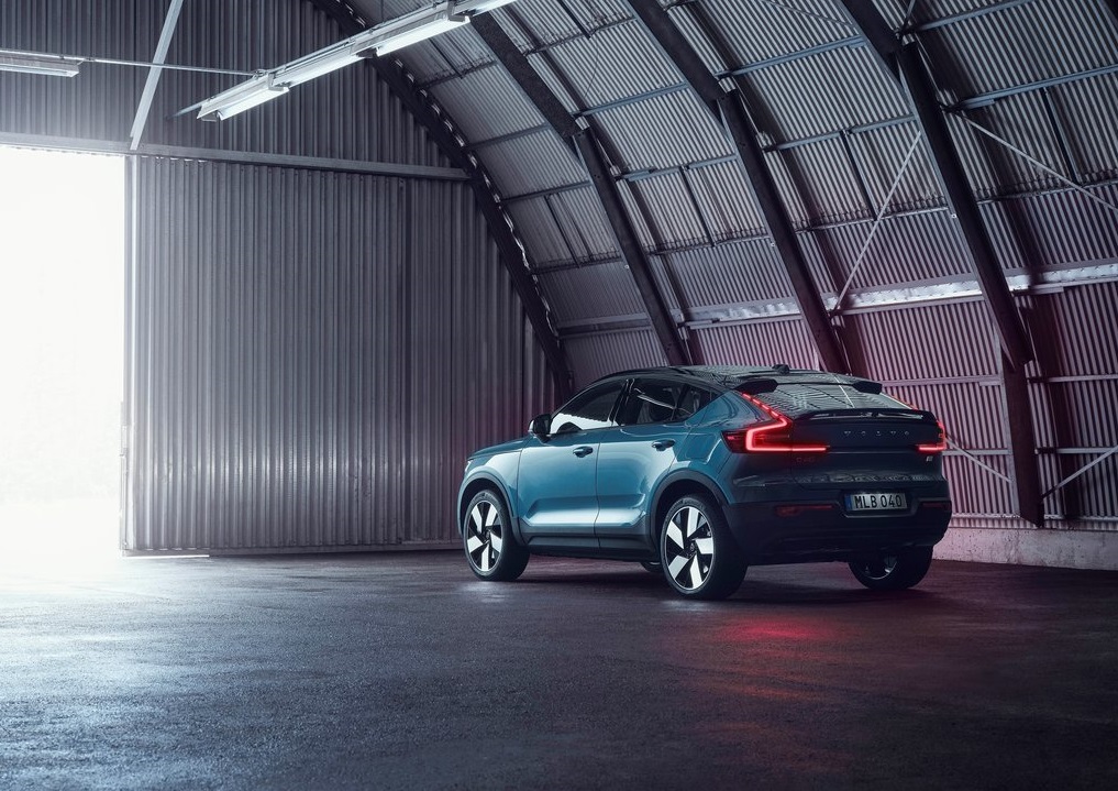 Niebieski SUV Volvo C40 z włączonymi tylnymi światłami stoi w metalowym garażu.