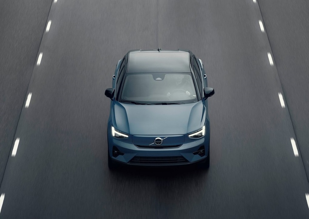 Niebieskie Volvo C40 jedzie środkowym pasem pustej, wielopasmowej drogi – widok z góry.