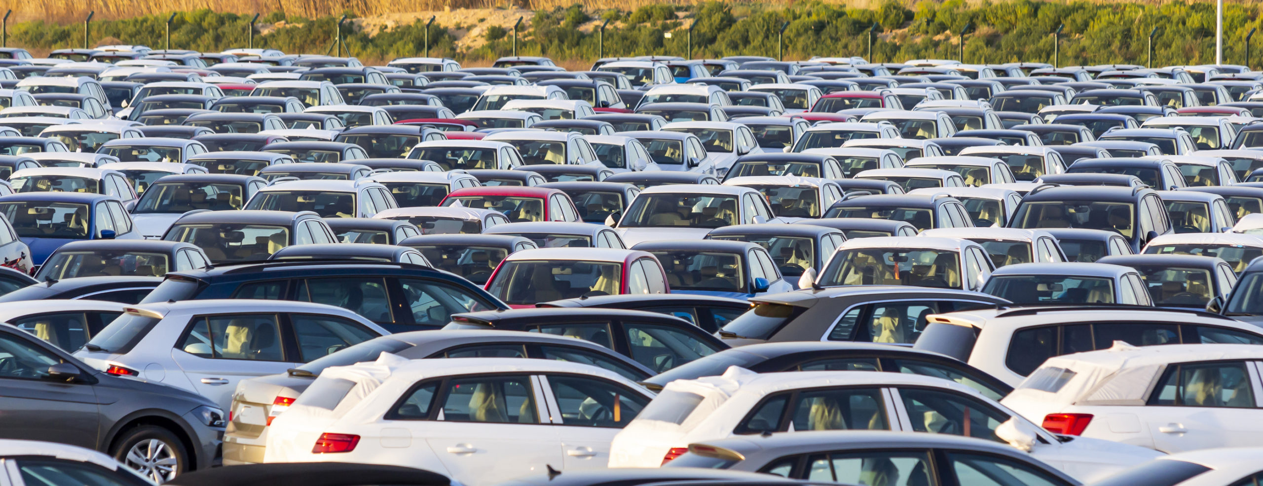 Parking pełen białych i srebrnych samochodów widziany z lotu ptaka – pytanie: kupić czy wynająć?.