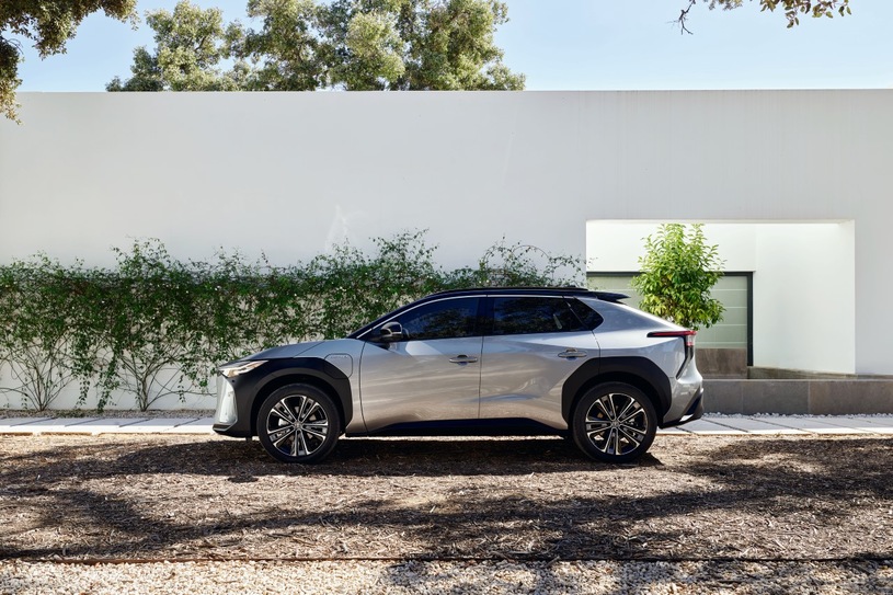 Srebrna Toyota bZ4X stoi na ziemi przed nowoczesnym białym budynkiem porośniętym pnączami i drzewami.