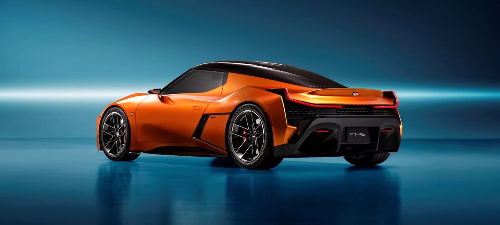 Pomarańczowa sportowa Toyota z czarnymi akcentami na niebieskiej, lustrzanej powierzchni.