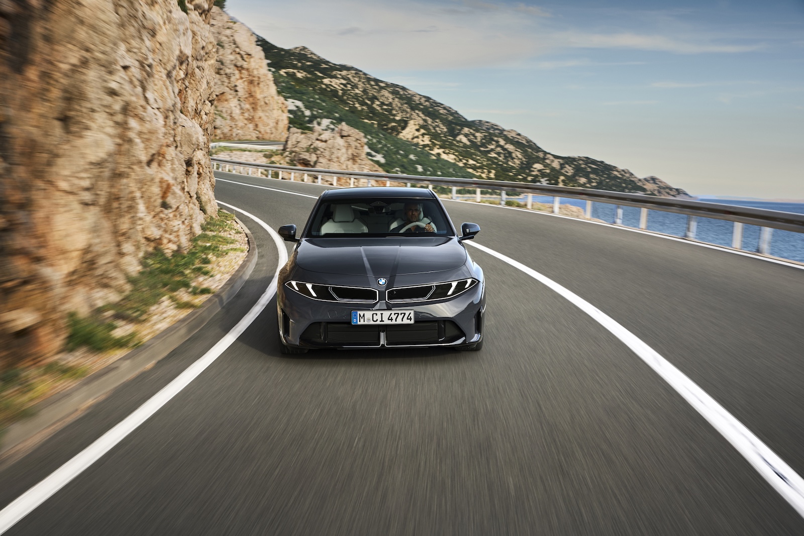 Czarne BMW jedzie krętą nadmorską drogą wśród skał pod błękitnym niebem.