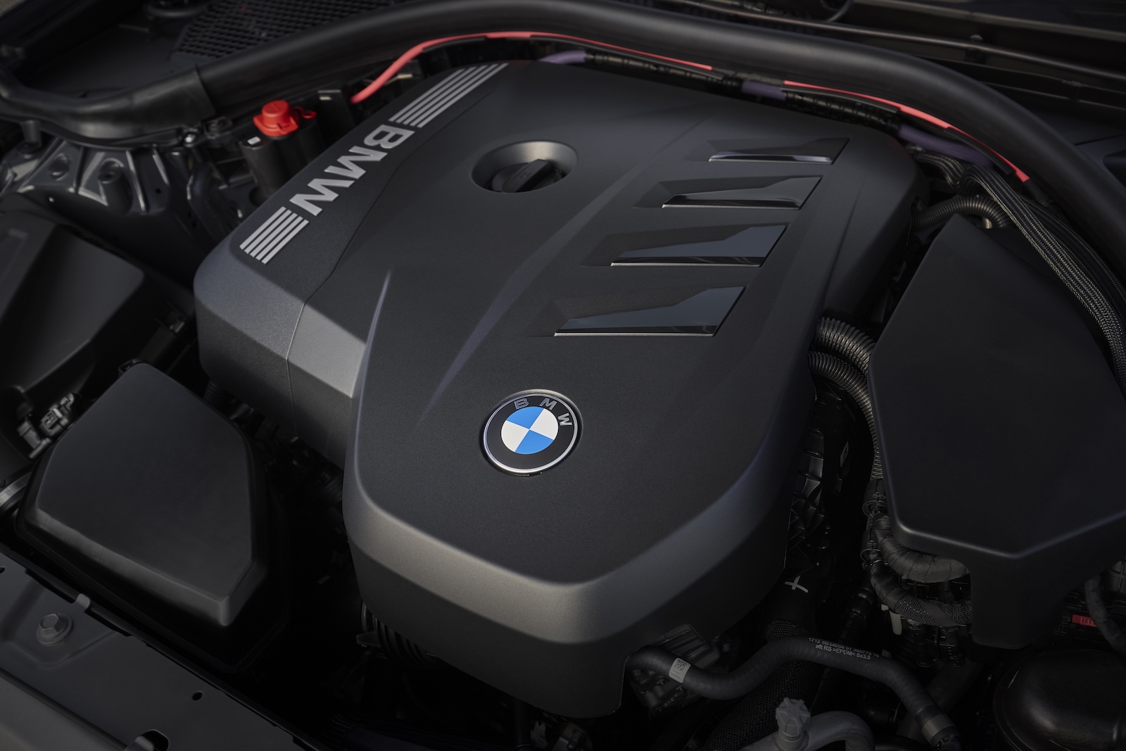 Detal BMW na pokrywie silnika – logo otoczone elementami komory silnika.