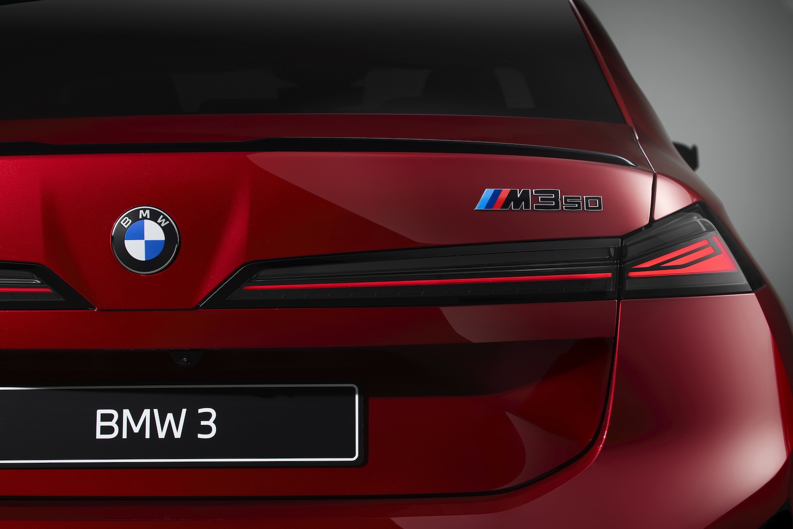 Tył czerwonego BMW 3 M350 z tylnymi światłami, logo BMW i emblematem M350.