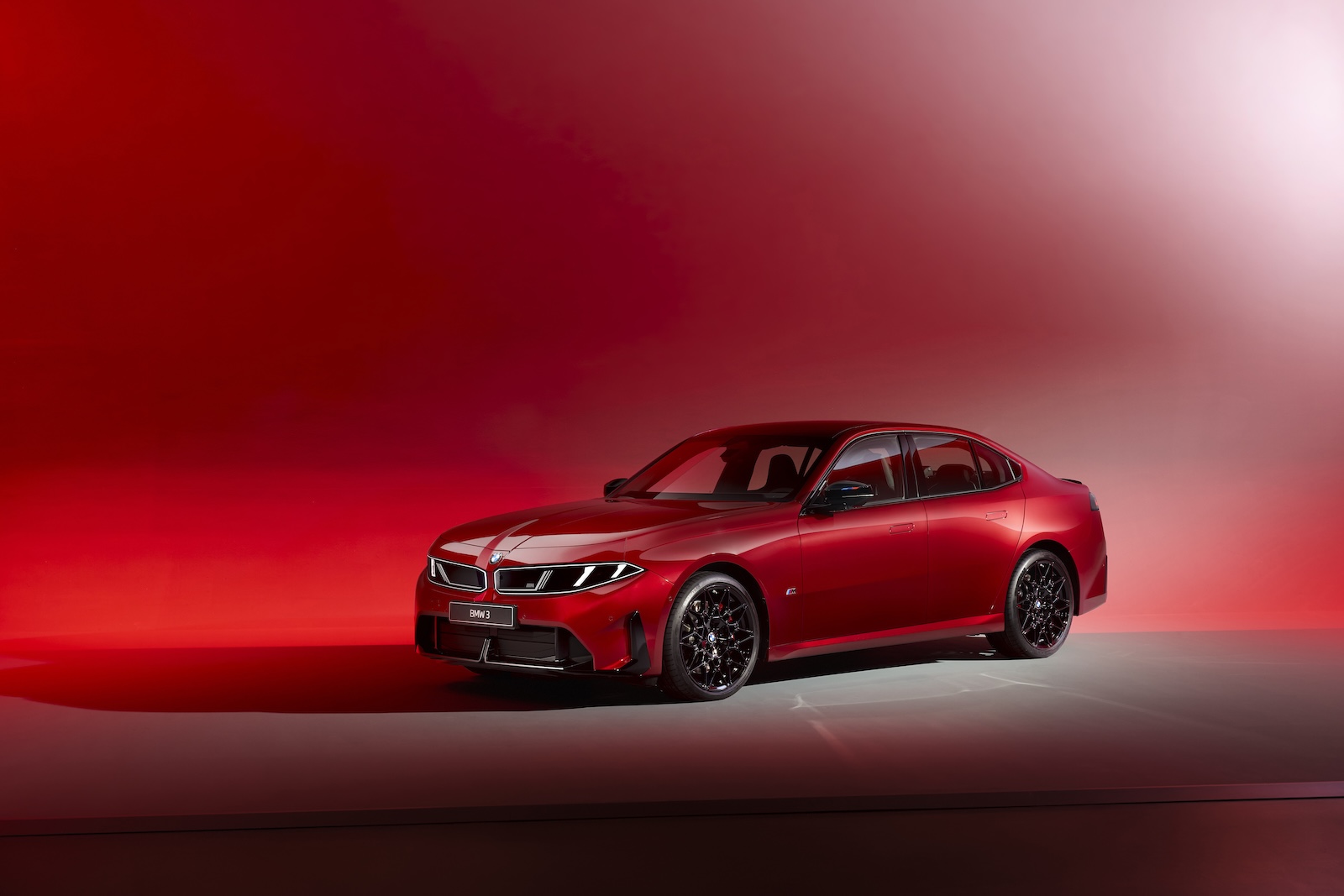 Czerwony sedan BMW na czarnych felgach w studiu fotograficznym z czerwonym tłem o gradientowym odcieniu.